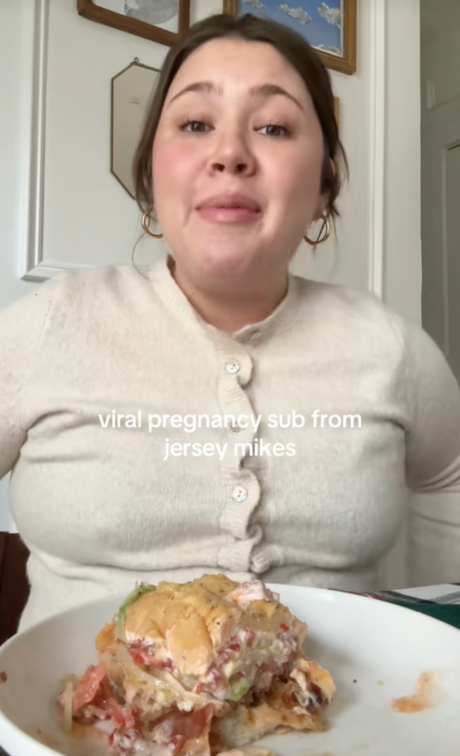Person smiling at the camera with a partially eaten sandwich on a plate. Text: "viral pregnancy sub from jersey mikes."