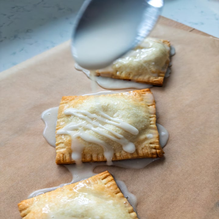 Icing being drizzled from a spoon over three rectangular pastries on parchment paper