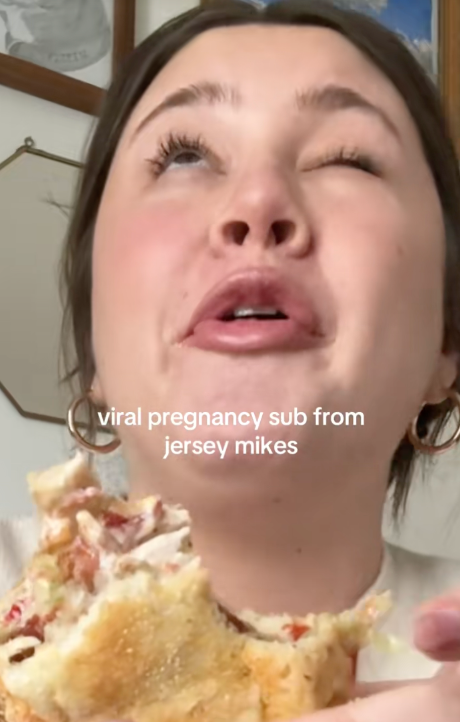 Person eating a sandwich labeled "viral pregnancy sub from Jersey Mike's," humorously reacting with wide eyes and a playful expression