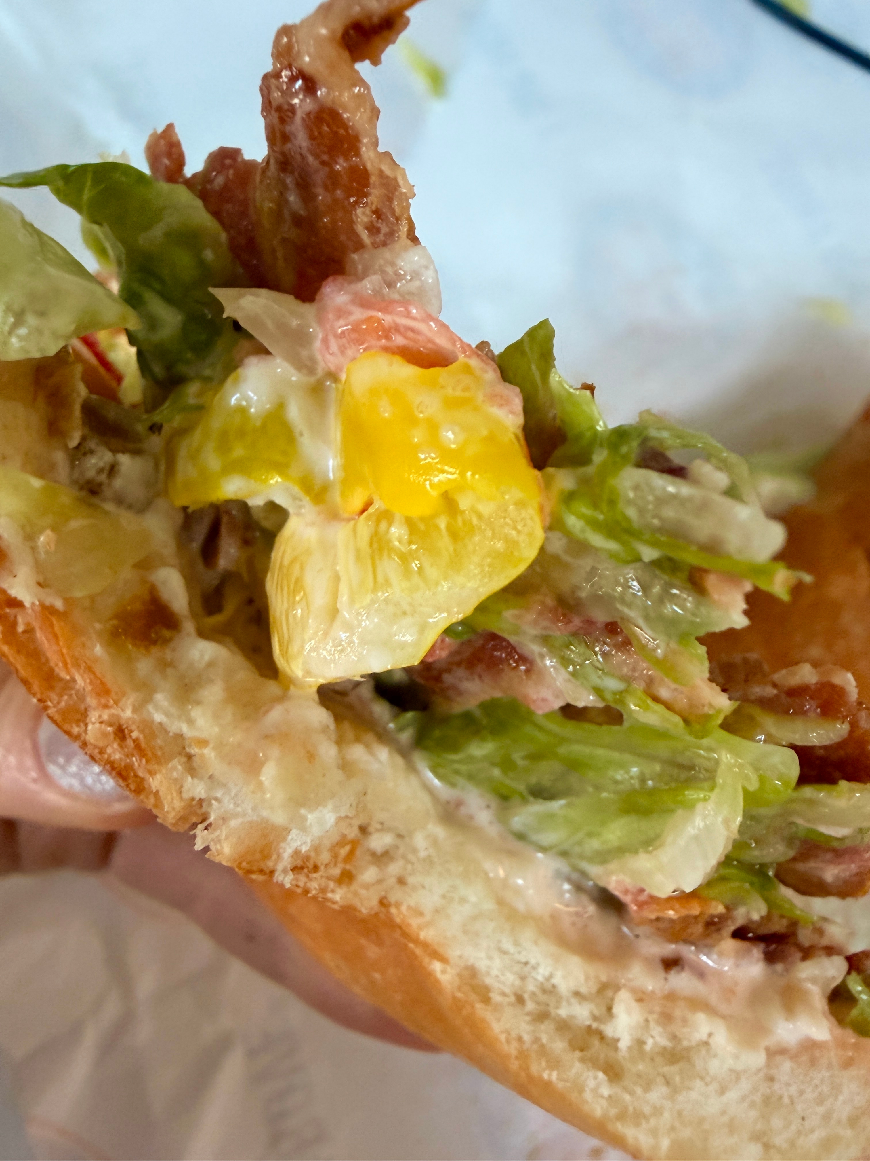 Close-up of a bitten sandwich with bacon, lettuce, egg, and mayonnaise filling exposed
