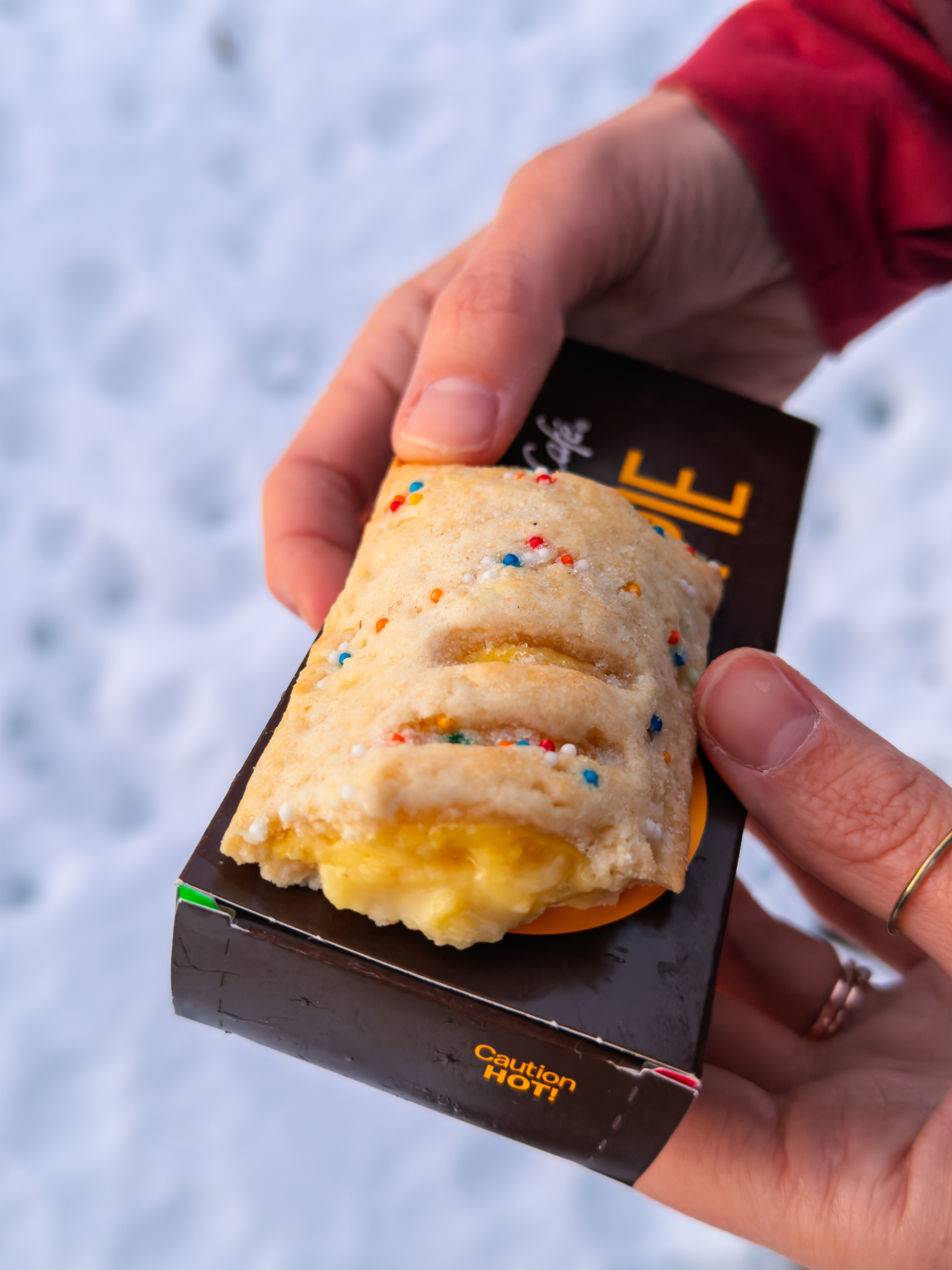 Hands holding a McDonald's pie with a caution label, set against a snowy background. Pie has sprinkled crust and visible filling