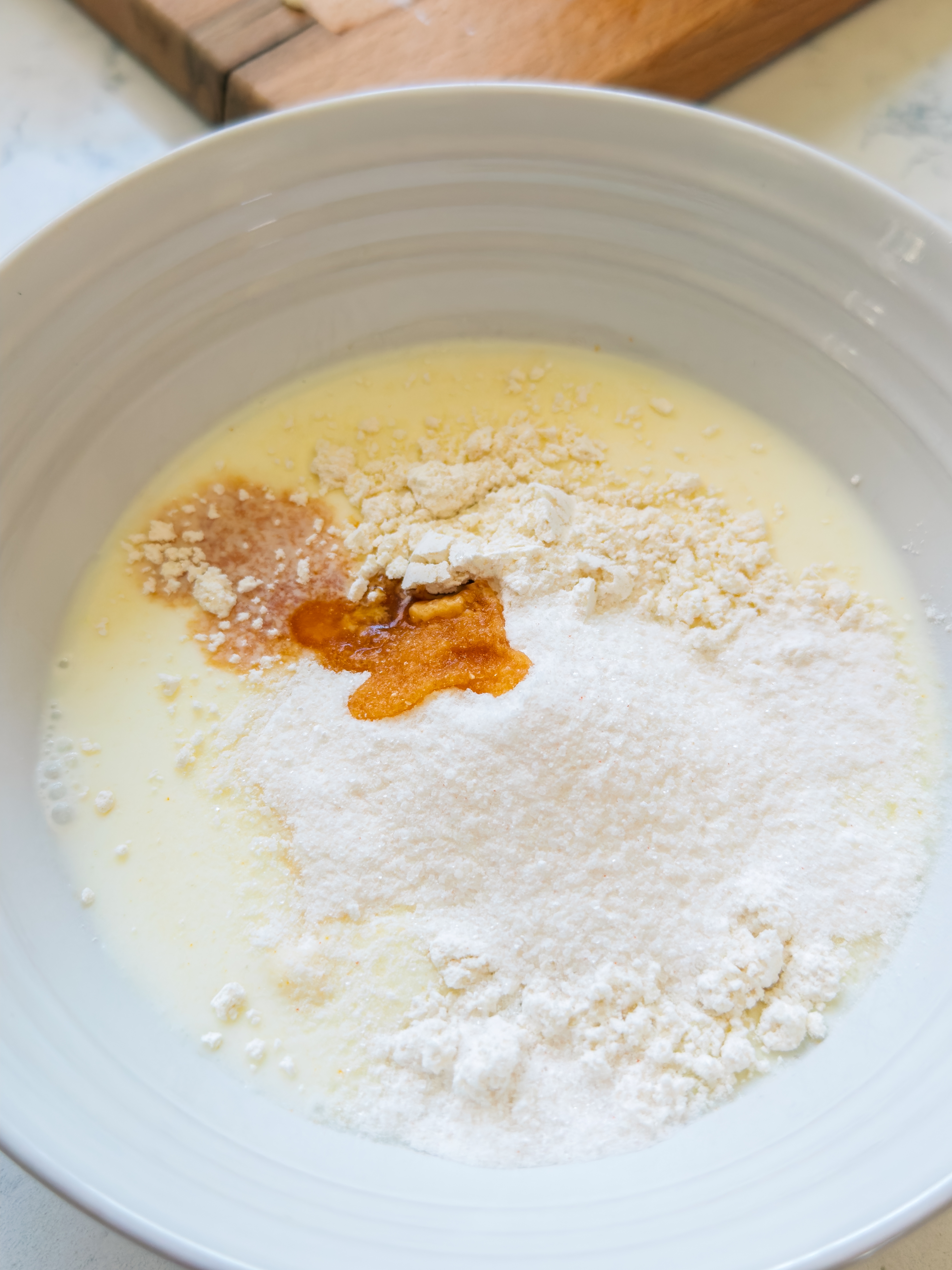 Bowl containing ingredients for baking, such as flour, sugar, and a liquid mixture, with a hint of vanilla