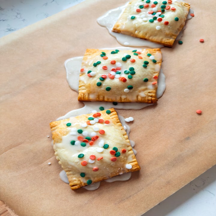 Three frosted pastries with festive sprinkles placed on a parchment-lined surface