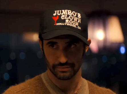 Person wearing a headdress with "Jumbo's Clown Room, Hollywood, CA" text, gazing intently. Background features blurred indoor lights