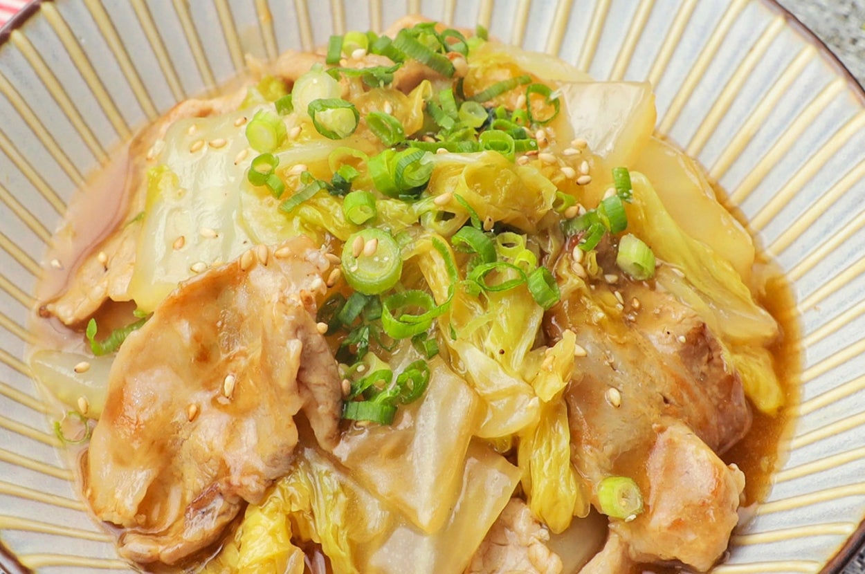 キャベツと豚肉の煮物が盛られた皿。刻んだネギとごまがトッピングされている。