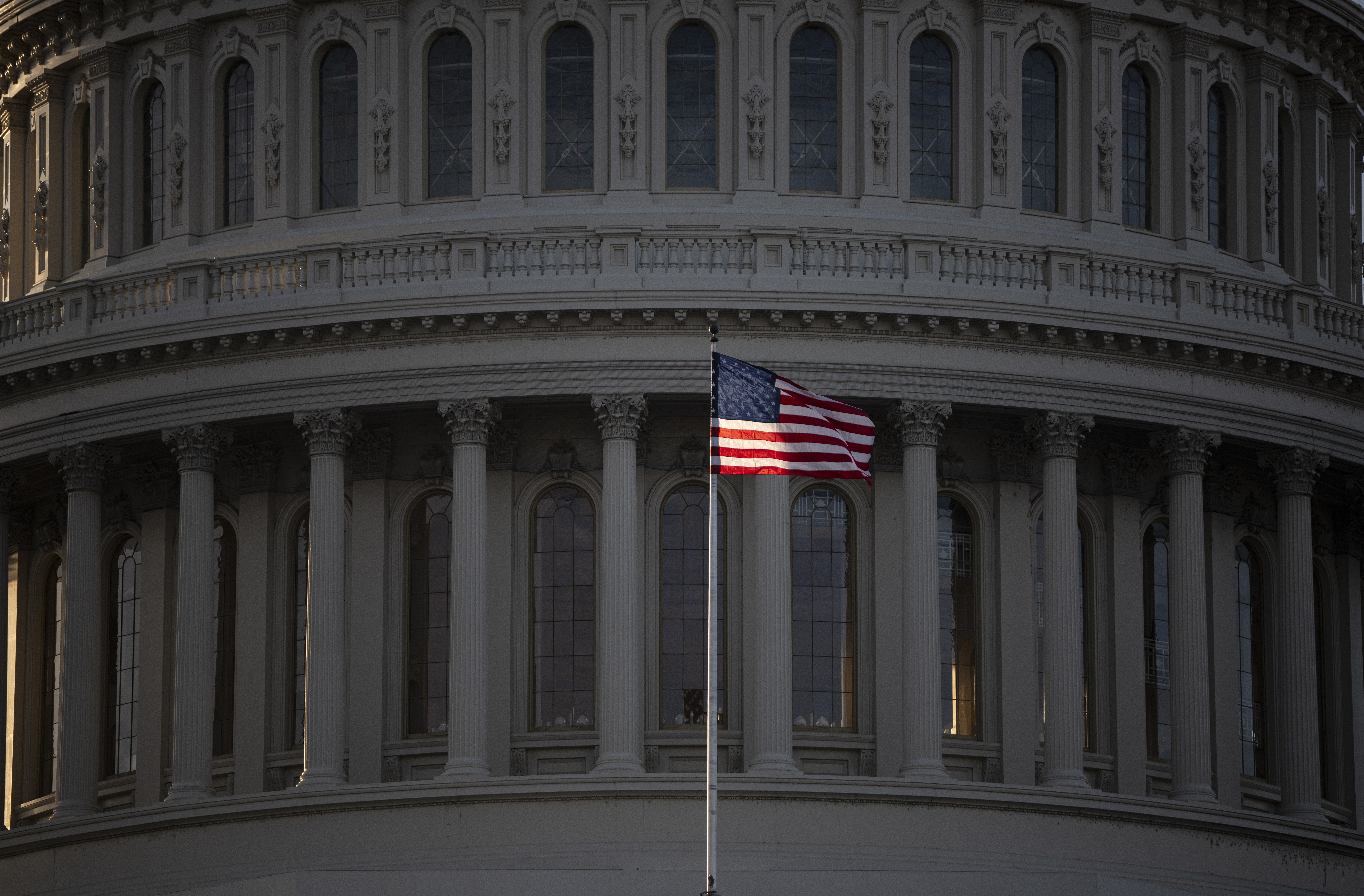 US Capitol-bygning med amerikansk flagg vaiende i forgrunnen. Klassisk arkitektur med søyler og vinduer