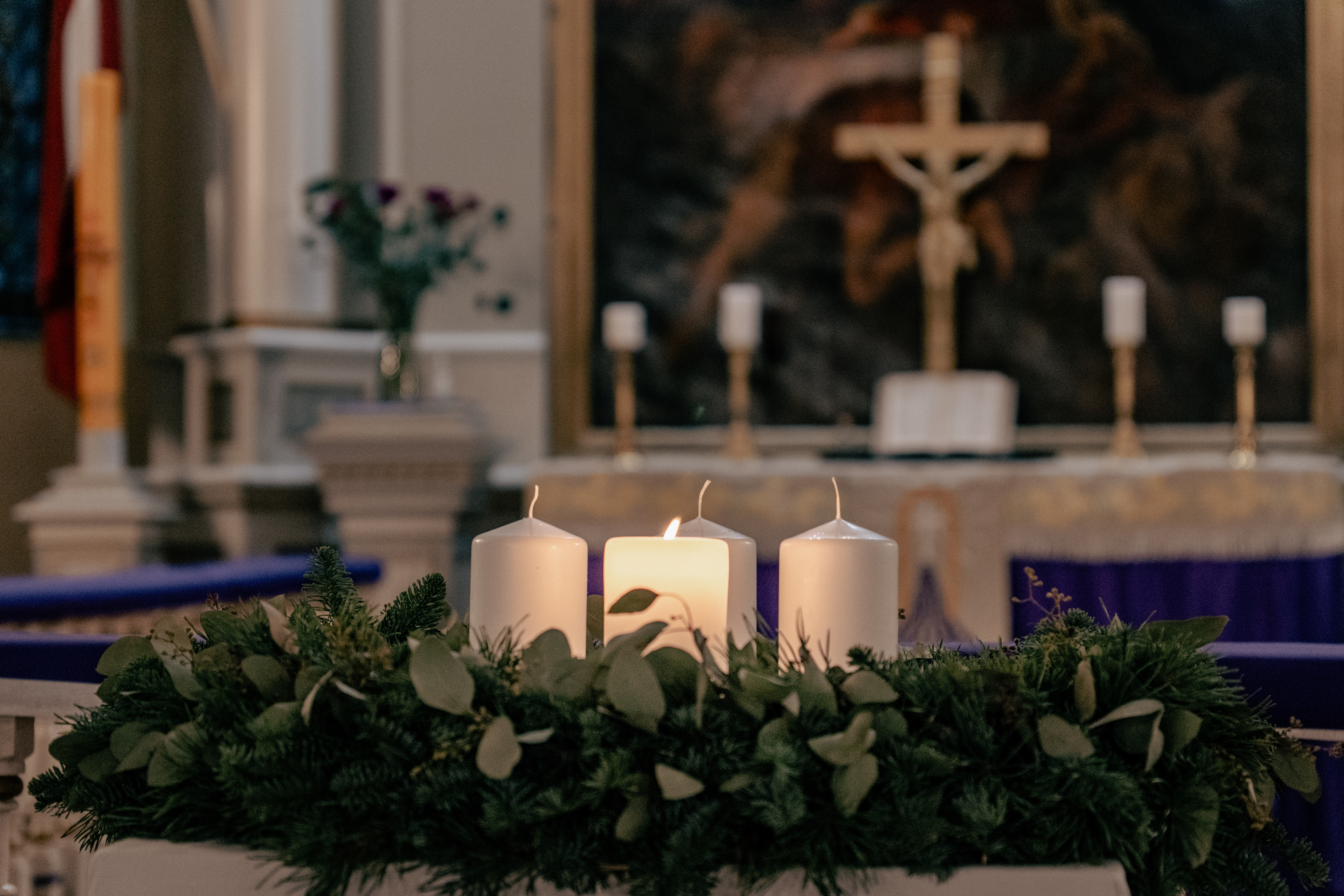 Lys tent på en adventskrans i kirkelige omgivelser, med et krusifiks og alter i bakgrunnen