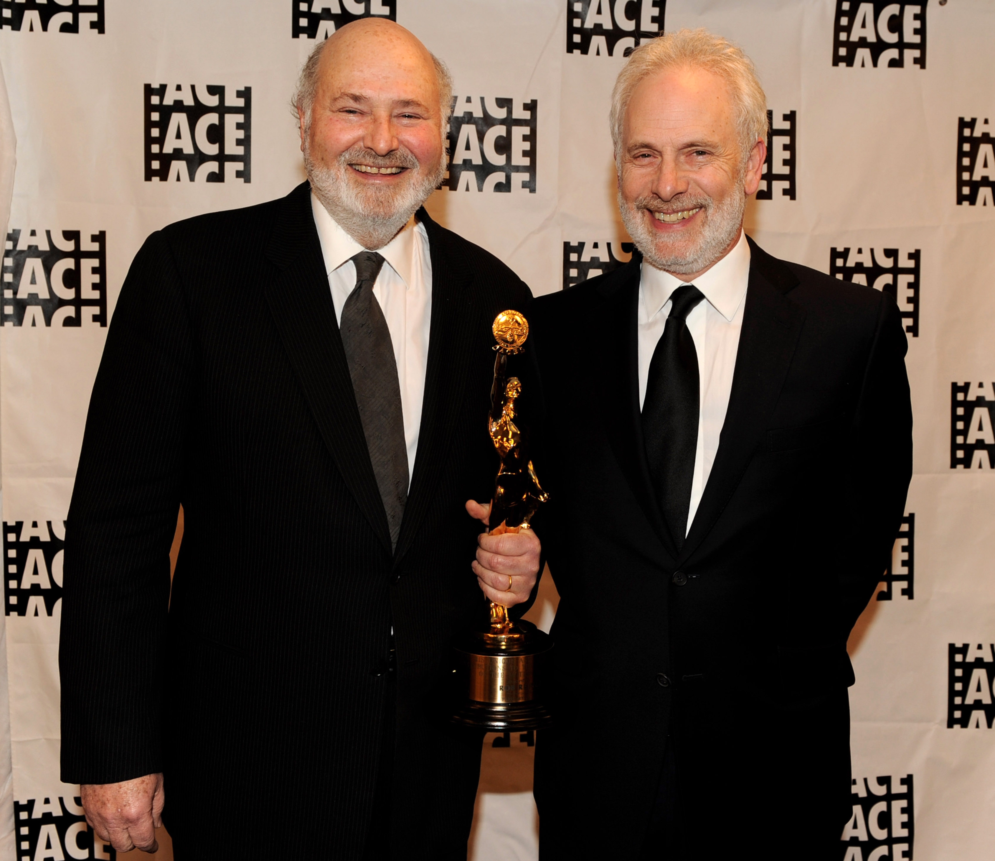 Two men successful suits connected a property backdrop, smiling, 1 holding an grant trophy