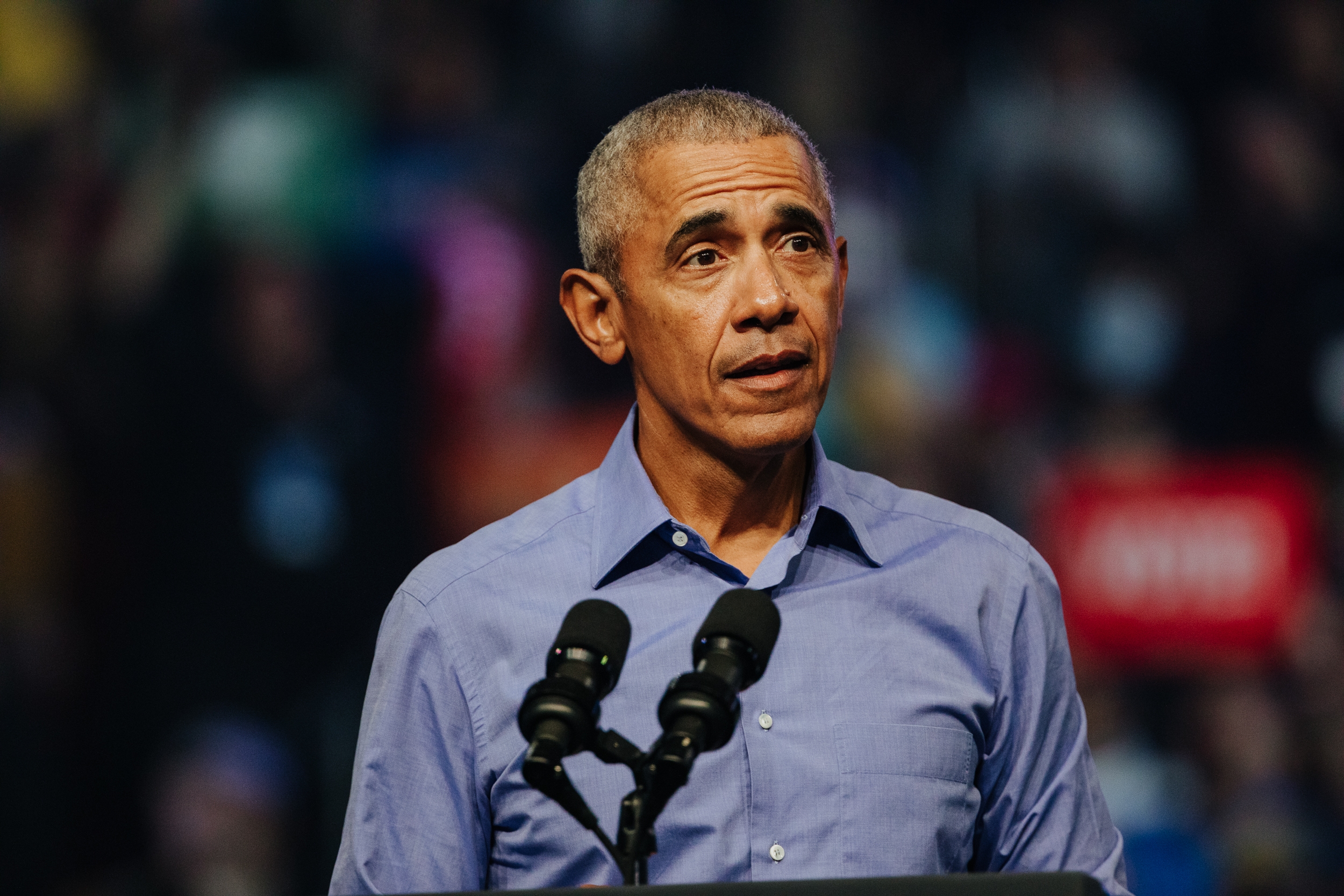 A antheral successful a button-up garment stands astatine a podium, speaking into 2 microphones astatine an lawsuit with a blurred assemblage successful the background