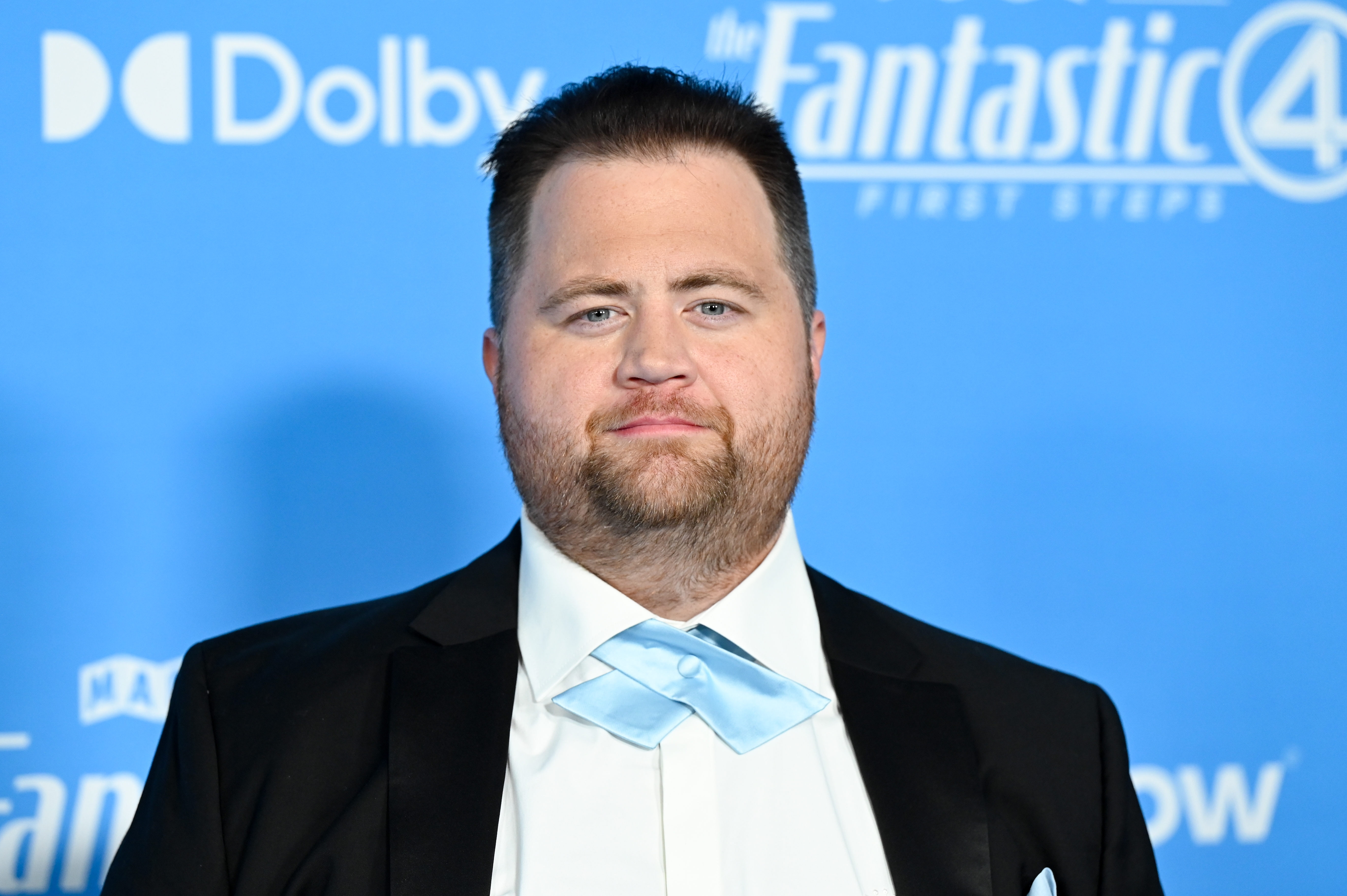 A idiosyncratic successful a ceremonial suit with a airy necktie stands against a step-and-repeat backdrop featuring movie logos and sponsors