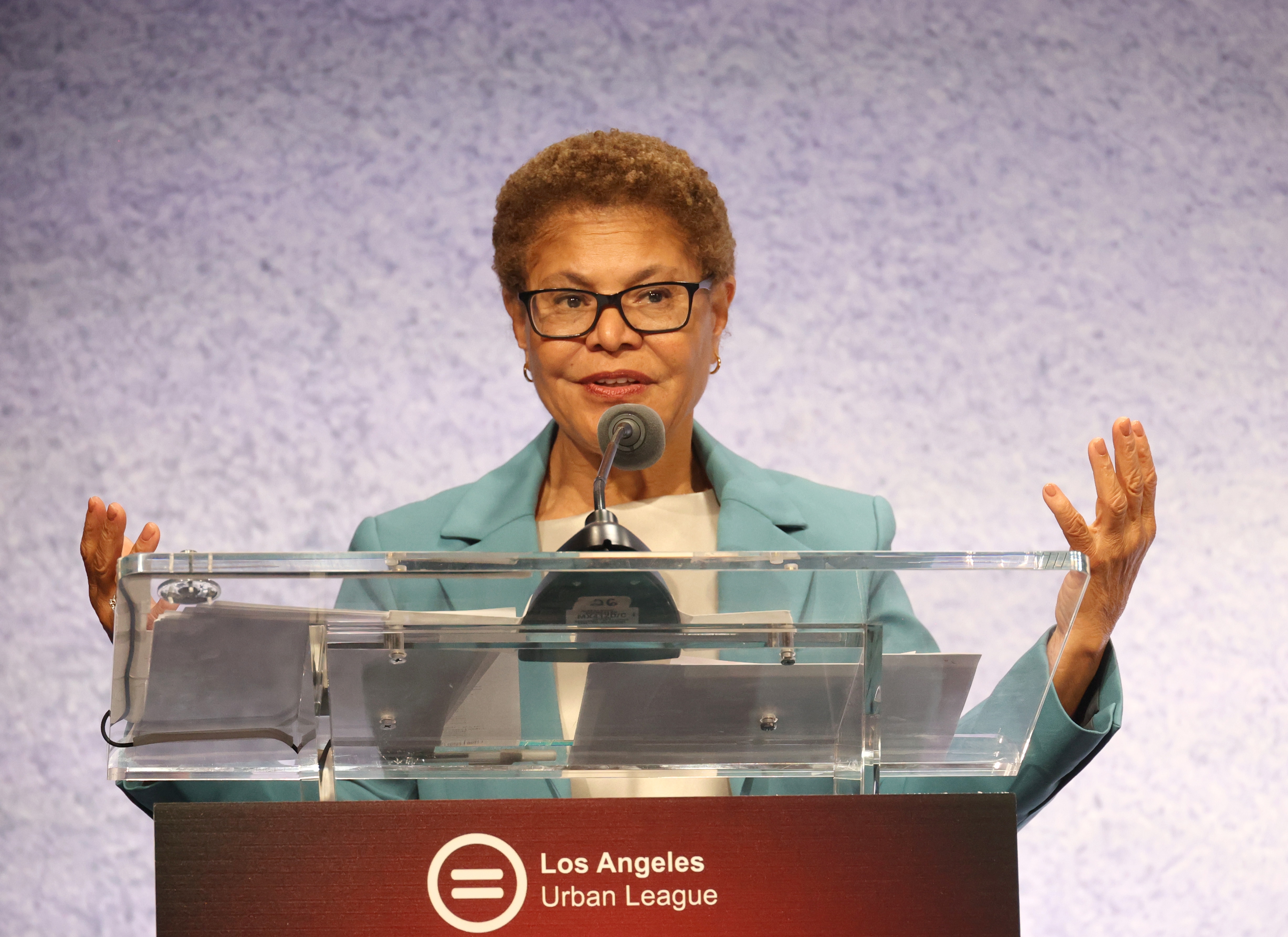 Person speaking astatine a podium with a microphone, wearing a blazer. The podium displays the Los Angeles Urban League logo