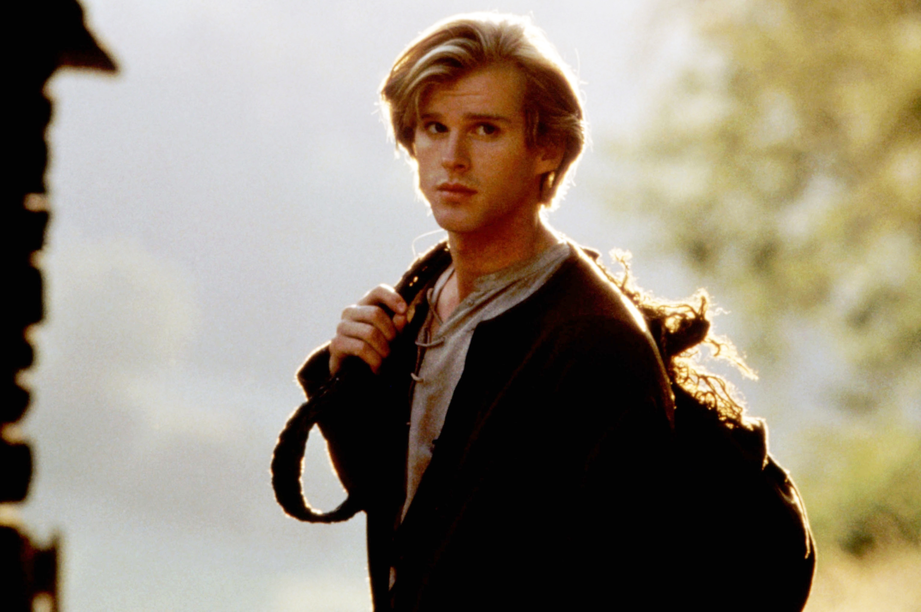 Person outdoors with shoulder-length hair, wearing a elemental outfit, carrying a enactment implicit the shoulder, gazing thoughtfully