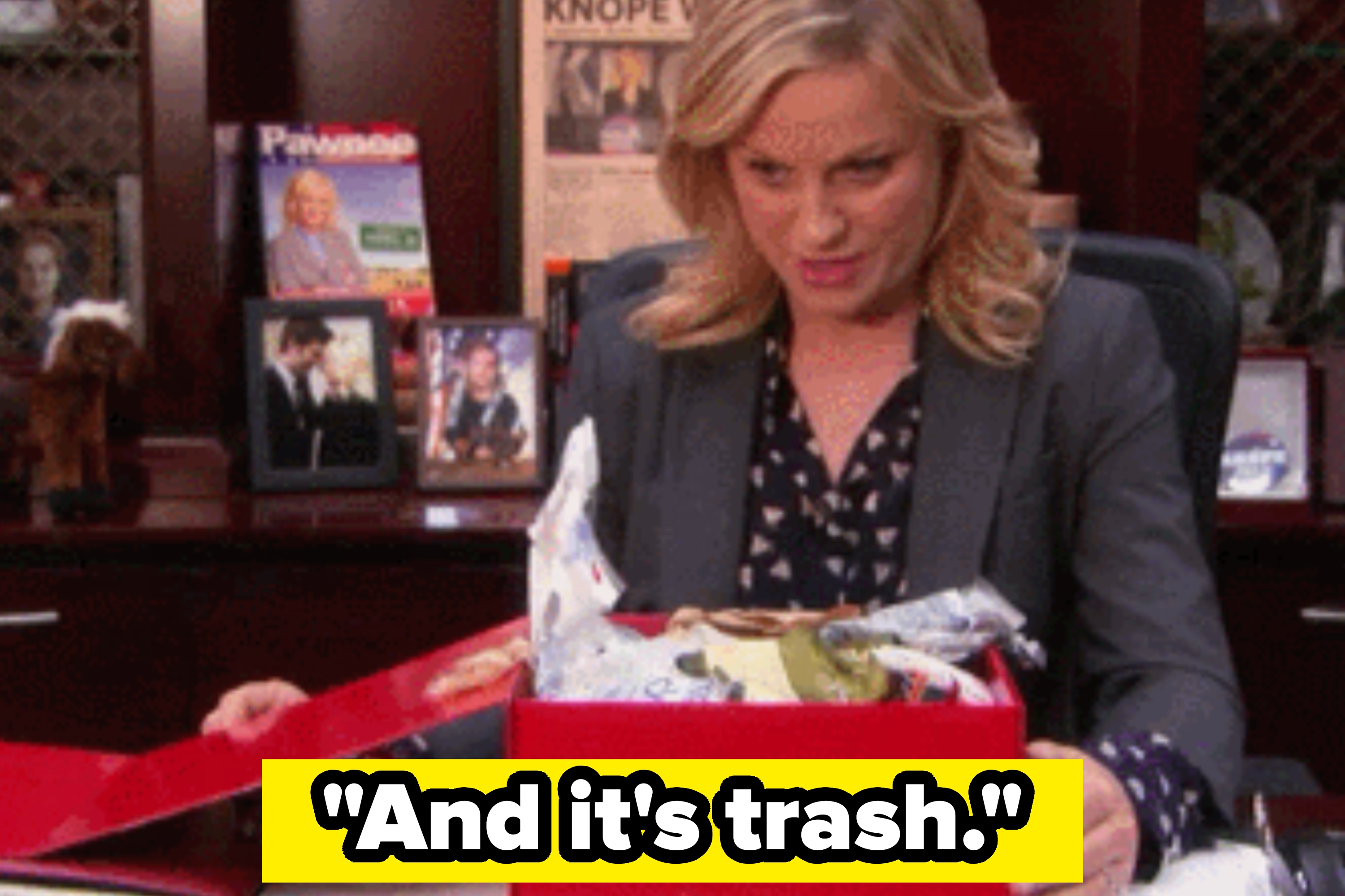 Woman in an office setting looking disapprovingly at a gift box with the caption "And it's trash." in bold letters below