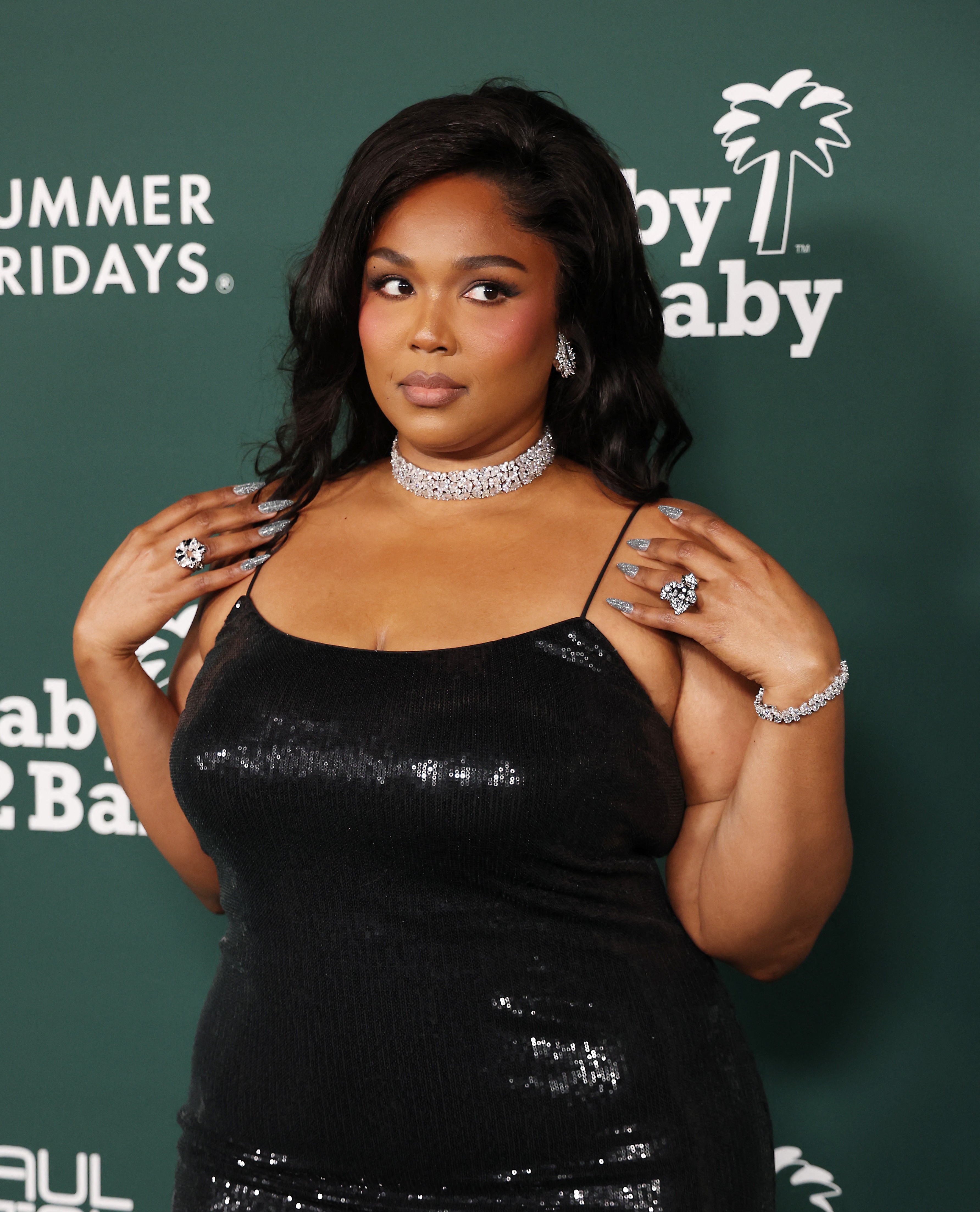 Person in a sequined dress poses on the red carpet, wearing sparkling jewelry including earrings, a necklace, and rings