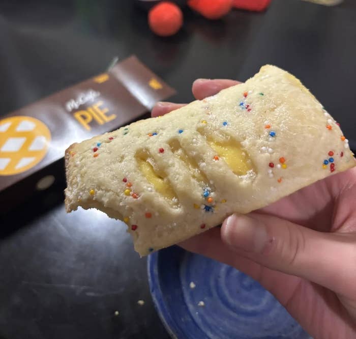 A hand holding a McDonald's pie with sprinkles, a bite taken out; pie box in background