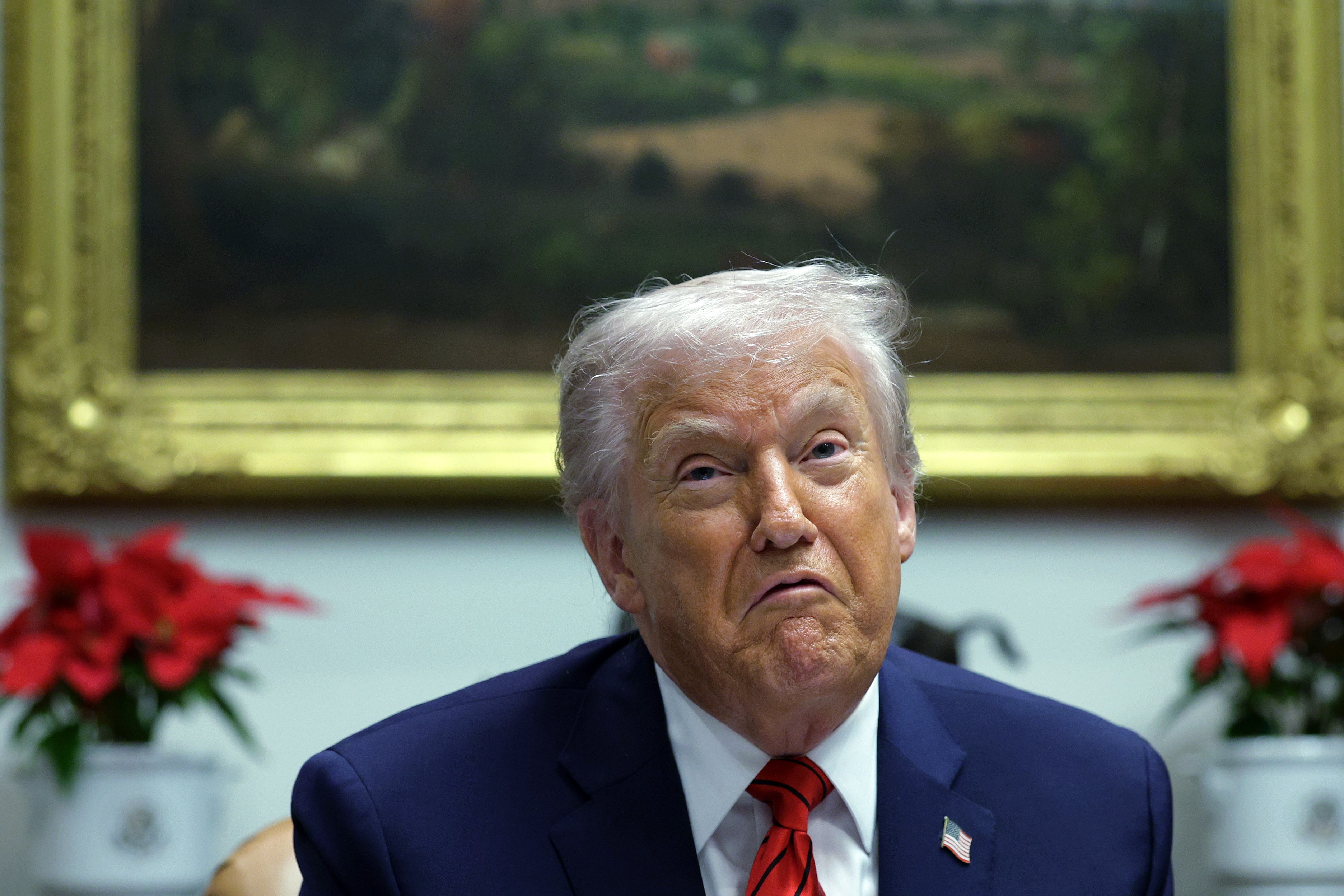 En person i dress med et mønstret slips ser ut til å reagere eller snakke i en innendørs setting med innrammet kunstverk i bakgrunnen