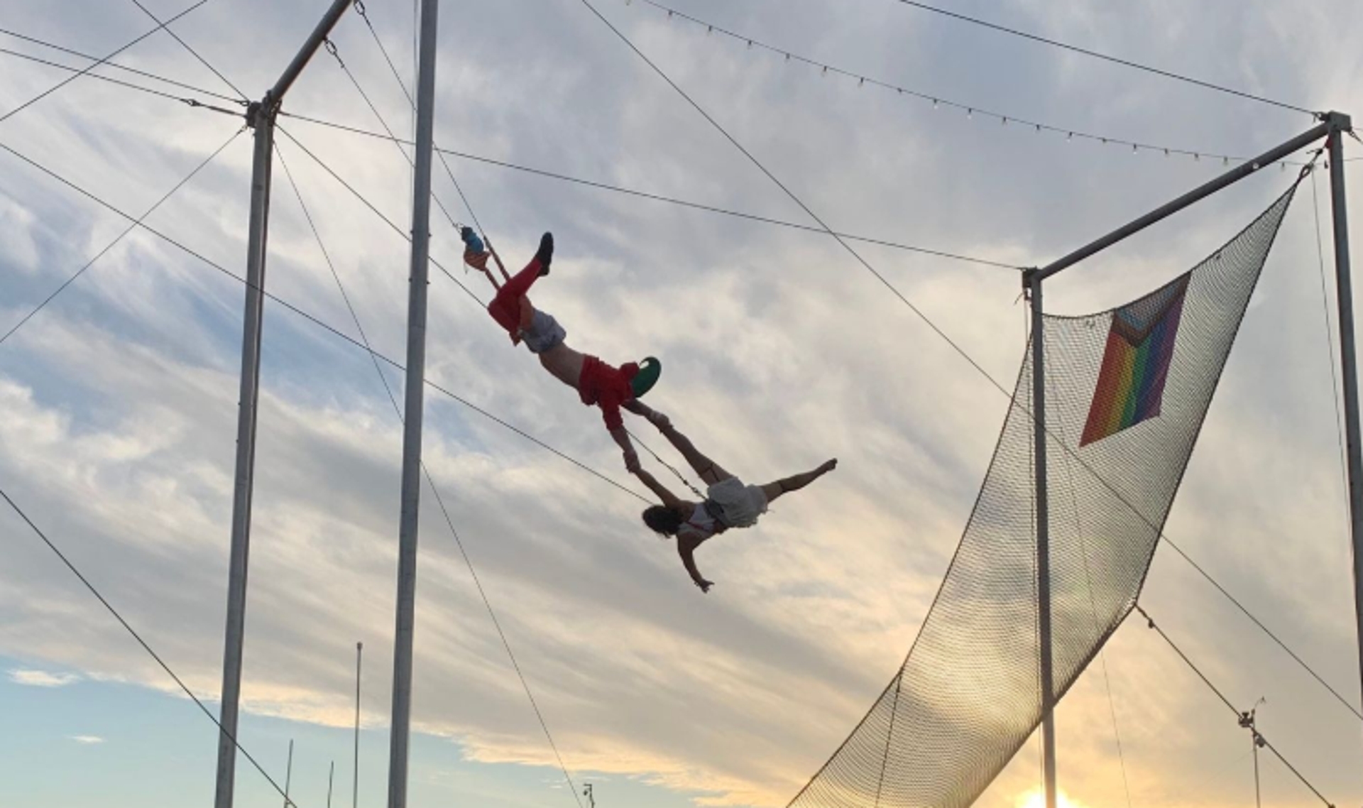 Two aerial performers connected  a trapeze execute a plaything  maneuver arsenic  the prima   sets, with a rainbow emblem  hanging nearby