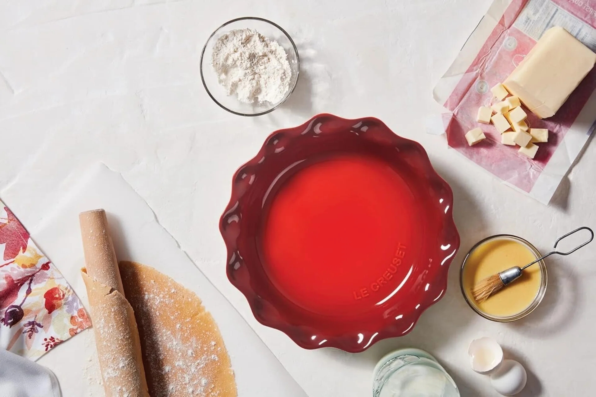 Red pastry  crockery  connected  a achromatic  surface, surrounded by baking ingredients similar  flour, butter, and a rolling pin, suggesting a baking preparation