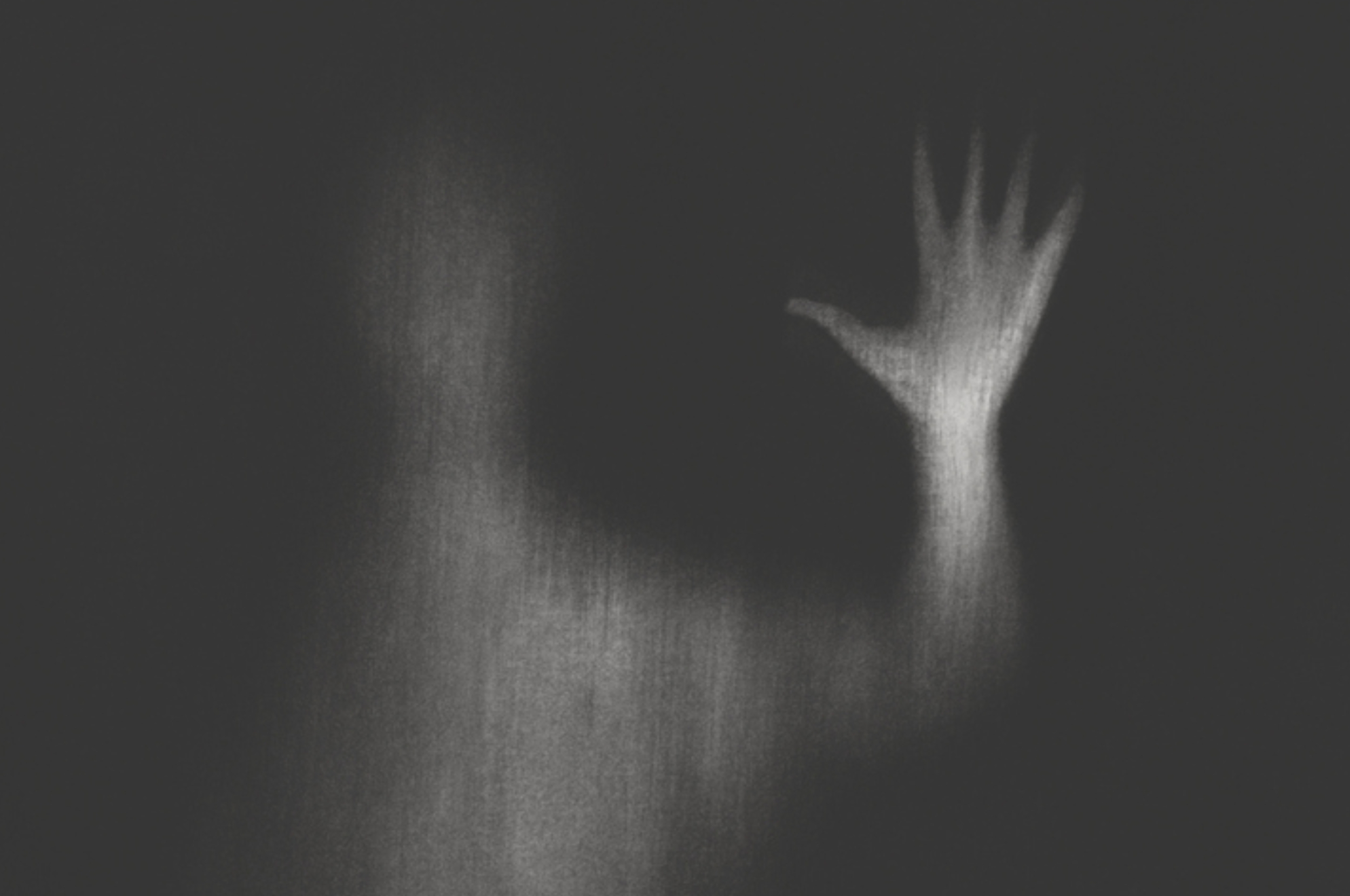 Uskarp silhuett av en person med hånden hevet, skaper en mystisk, eterisk effekt mot en mørk bakgrunn