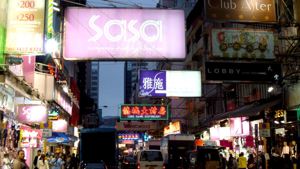 Et yrende urbant gatebilde med mange opplyste skilt og butikkfronter, som viser et livlig shoppingområde