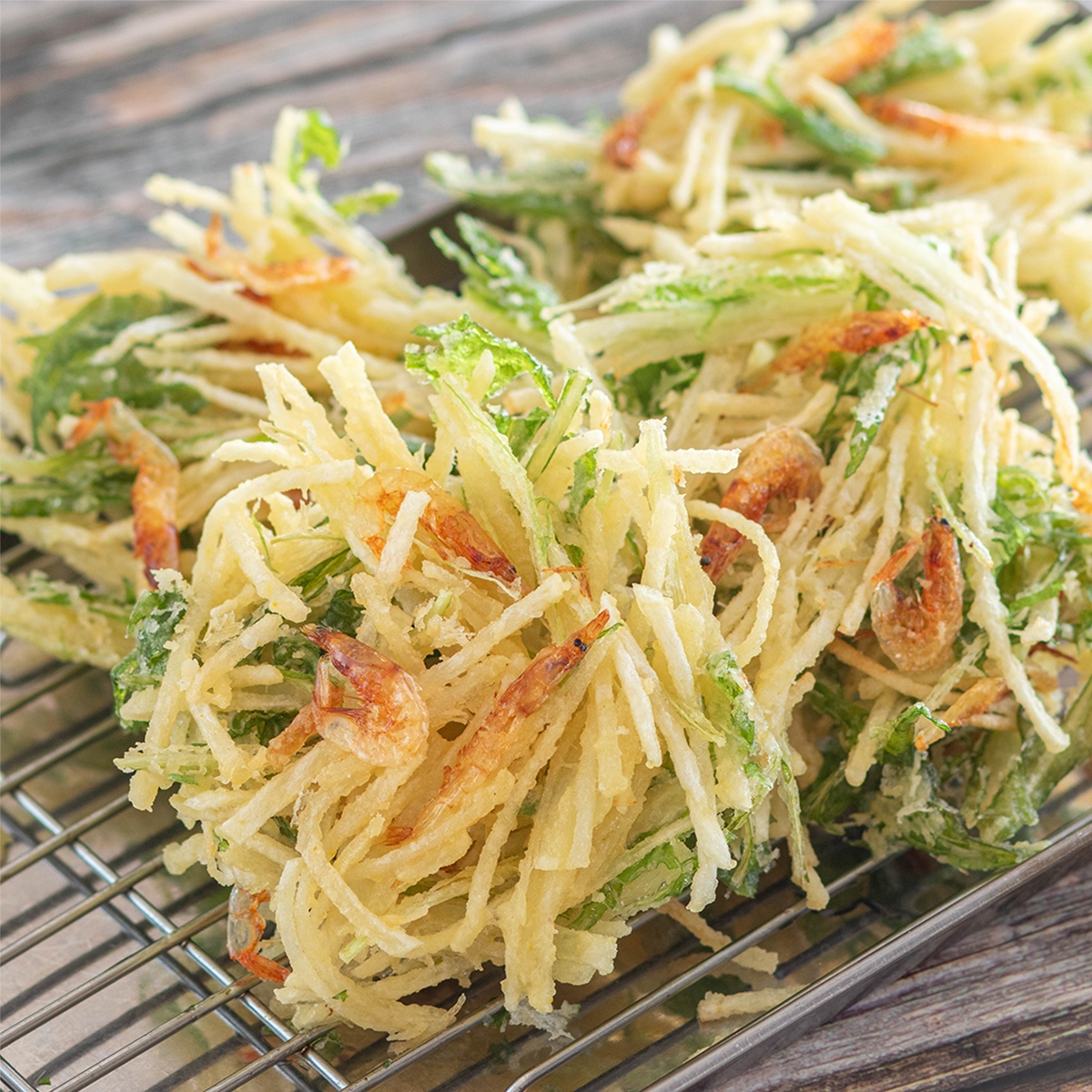 かき揚げのクローズアップ画像。野菜とエビが見られ、ワイヤーラックの上に置かれている。