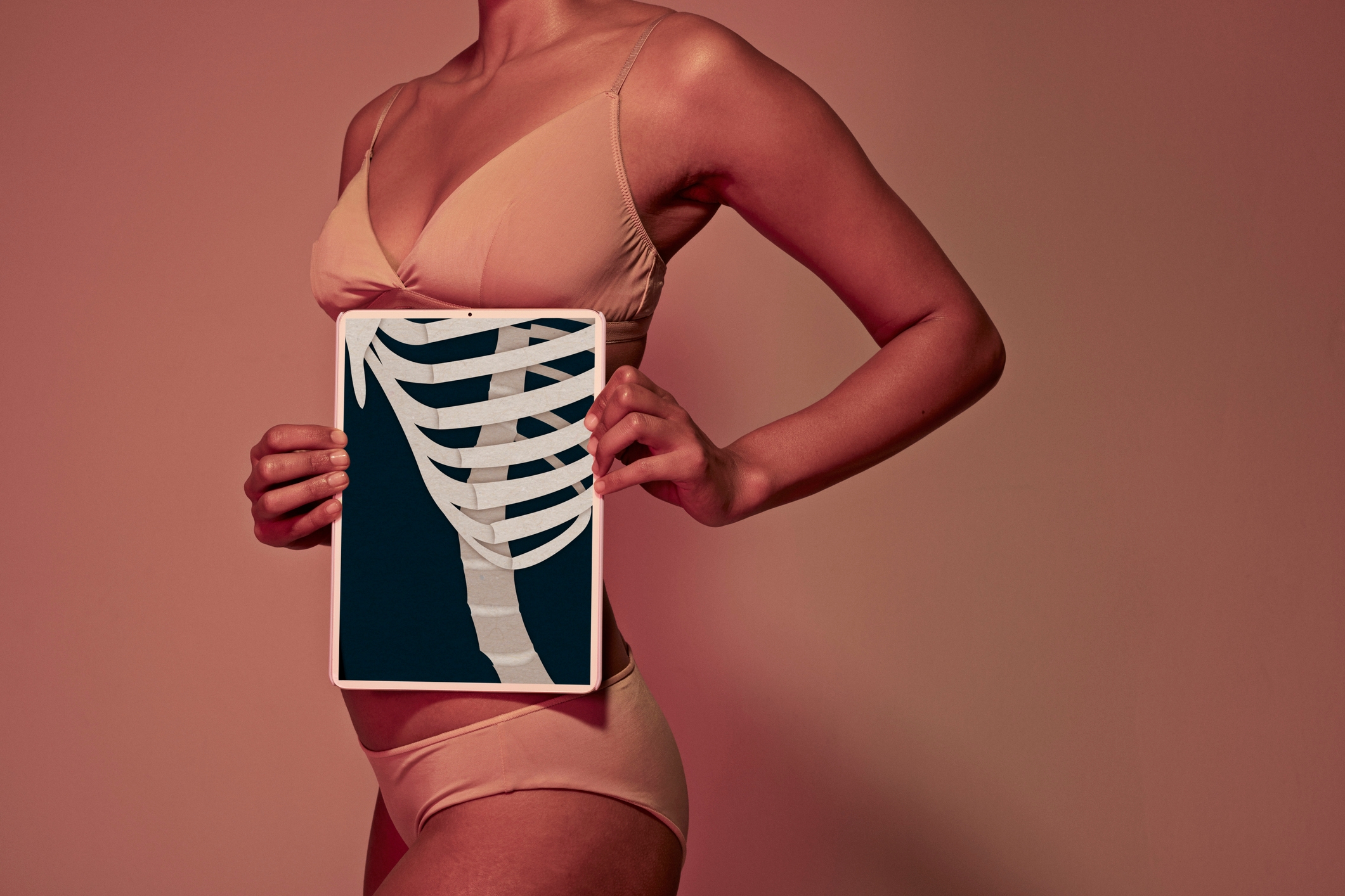 Person successful a bikini holding a tablet displaying an X-ray representation of ribs successful beforehand of their torso