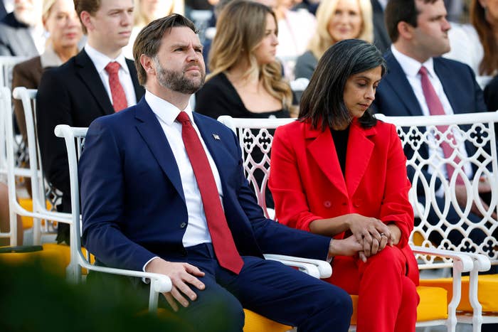 A antheral   successful  a suit   holds hands with a pistillate   successful  a stylish suit   during a ceremonial  outdoor event, surrounded by seated people