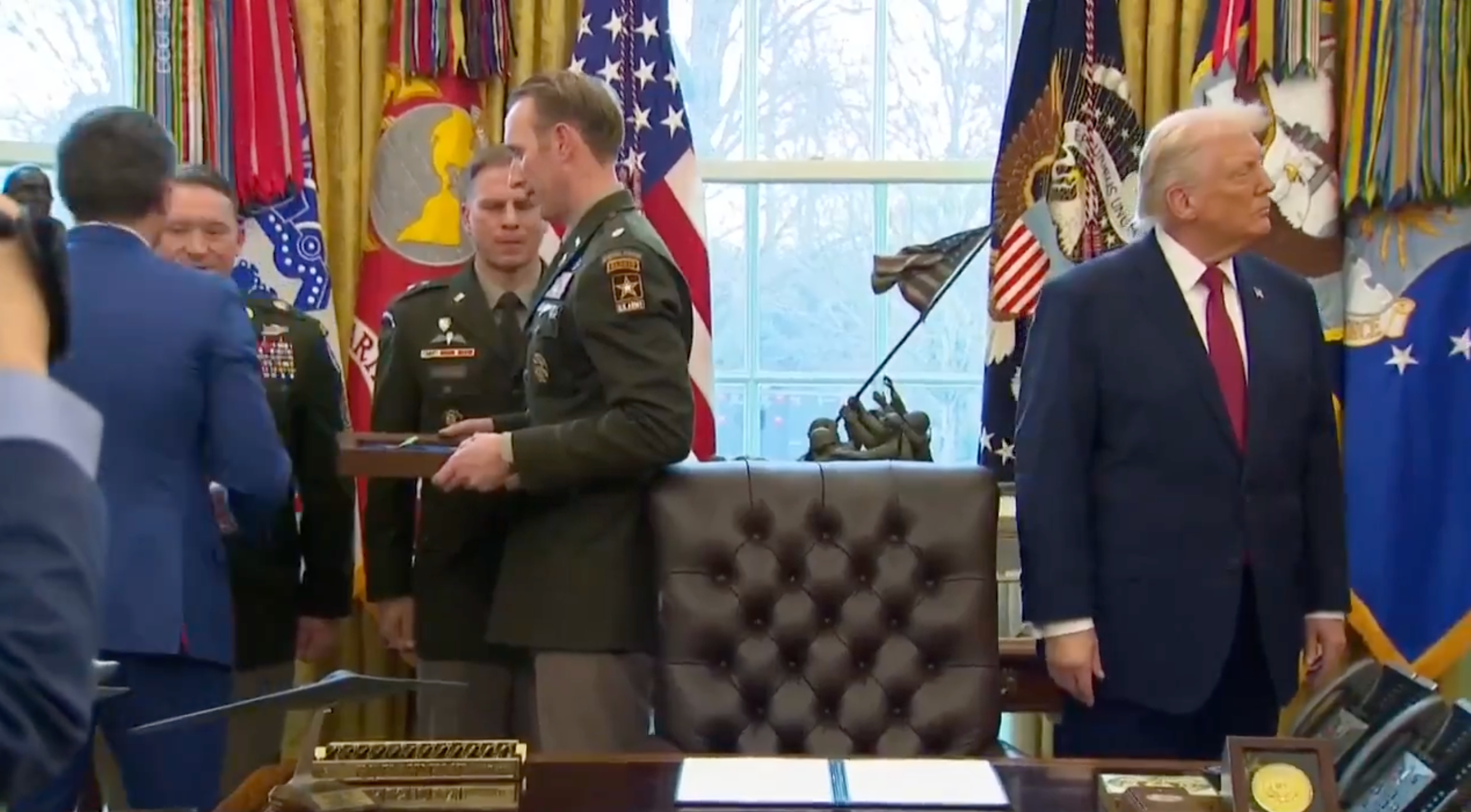 A radical of subject officials successful azygous contiguous a framed point to a idiosyncratic successful a suit successful a ceremonial bureau setting. A antheral successful a suit observes nearby