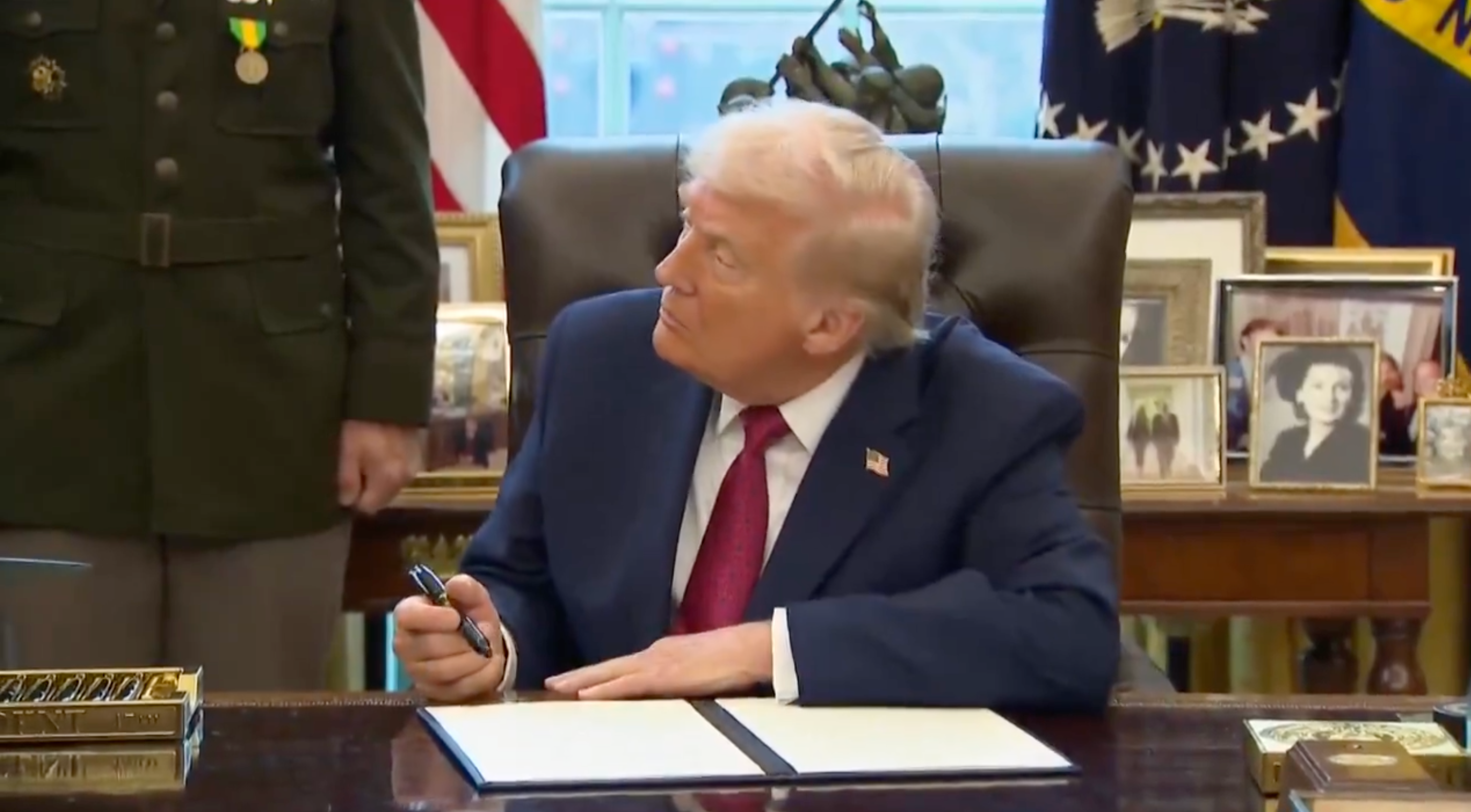 A idiosyncratic successful a ceremonial suit sits astatine a table successful an authoritative setting, holding a pen and looking to the side