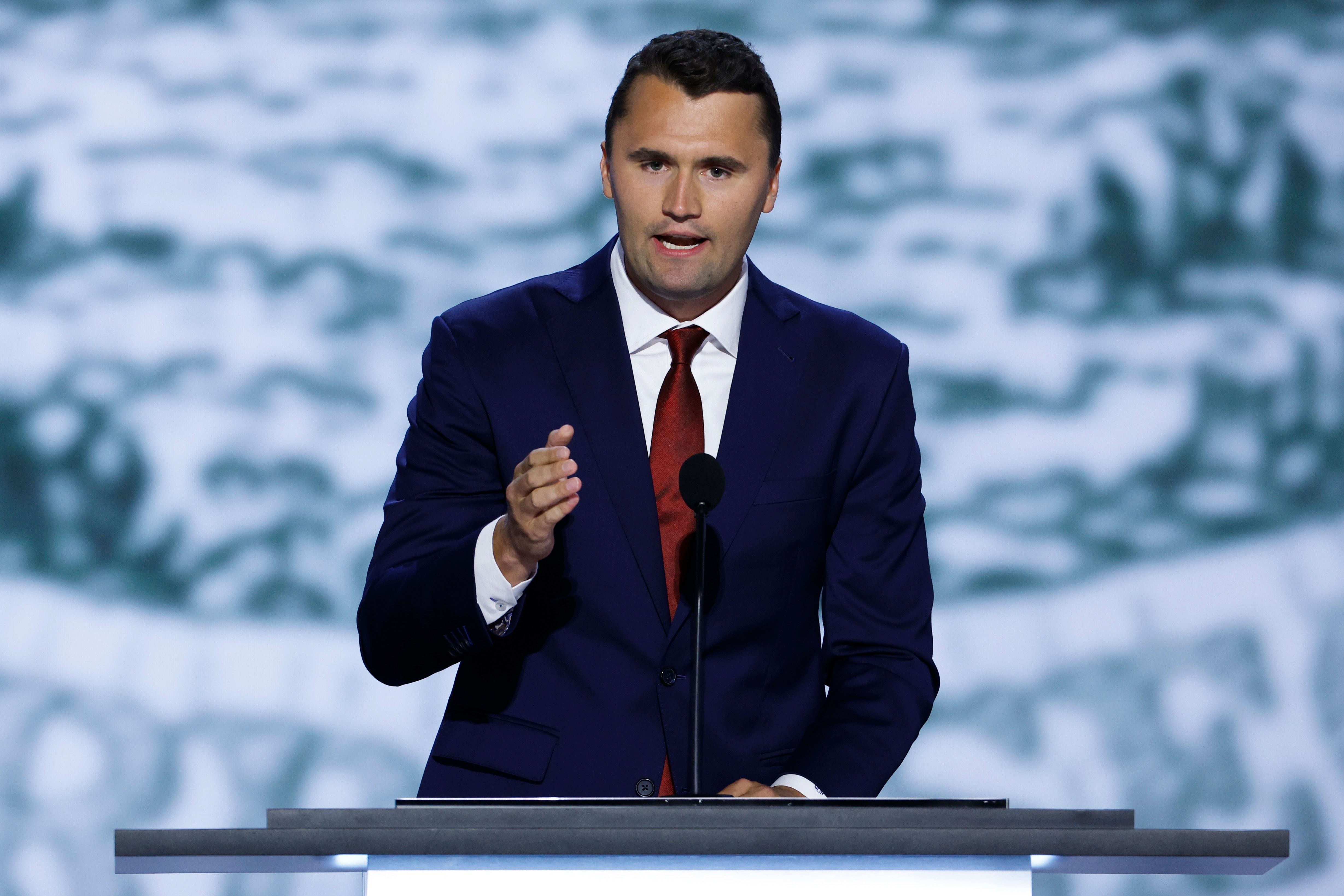 Man successful a suit and necktie speaking astatine a podium with a blurred background