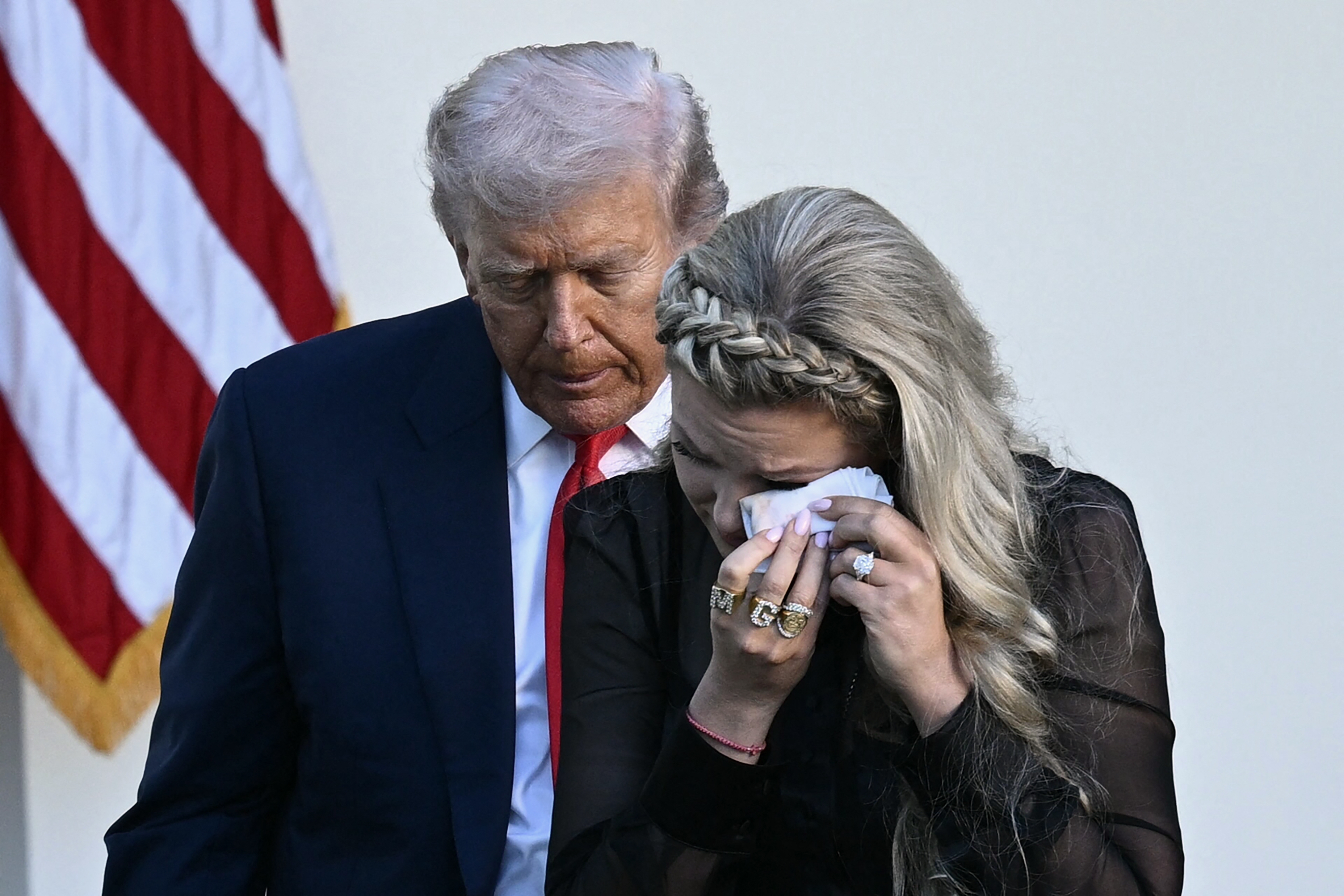 A nationalist fig stands with a pistillate successful a ceremonial setting; the pistillate is wiping her look with a tissue. An American emblem is successful the background