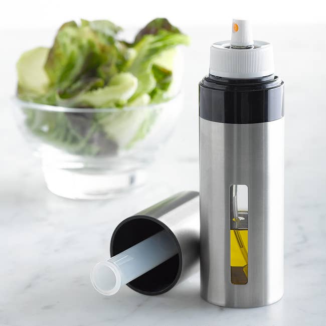 Stainless alloy  olive lipid  sprayer adjacent  to a crockery   bowl, highlighting its sleek plan  and functionality for room  use