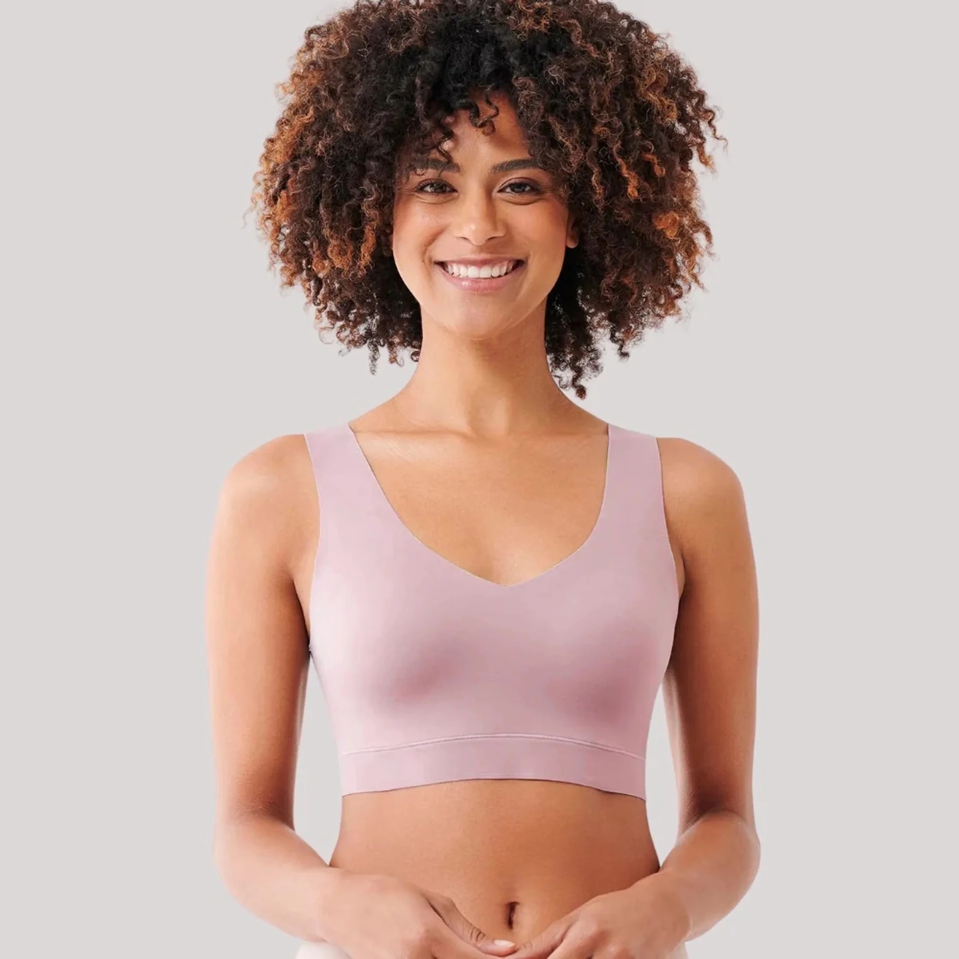 Person smiling, wearing a seamless, sleeveless undergarment with a V-neck, suitable for comfortableness and support