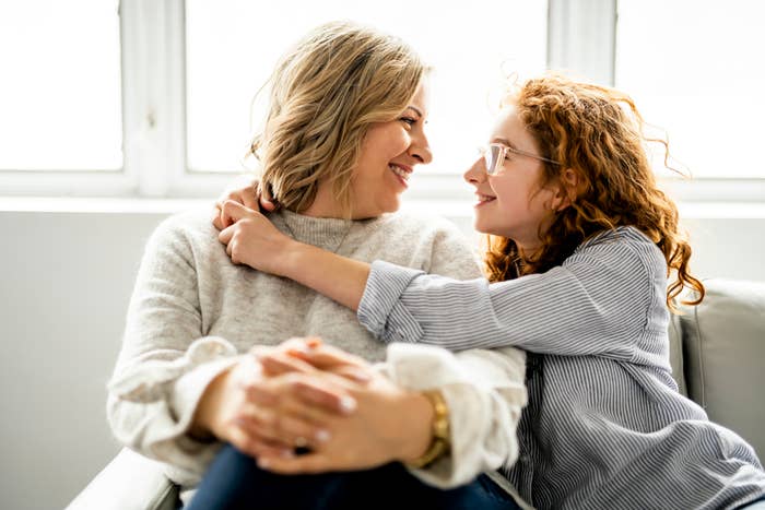Two radical   sitting connected  a couch, smiling astatine  each   different   warmly. One has curly hairsbreadth  and glasses, and the different   has wavy hair