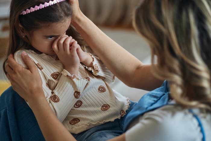 Child being comforted by an adult, looking concerned, held mildly  connected  a lap
