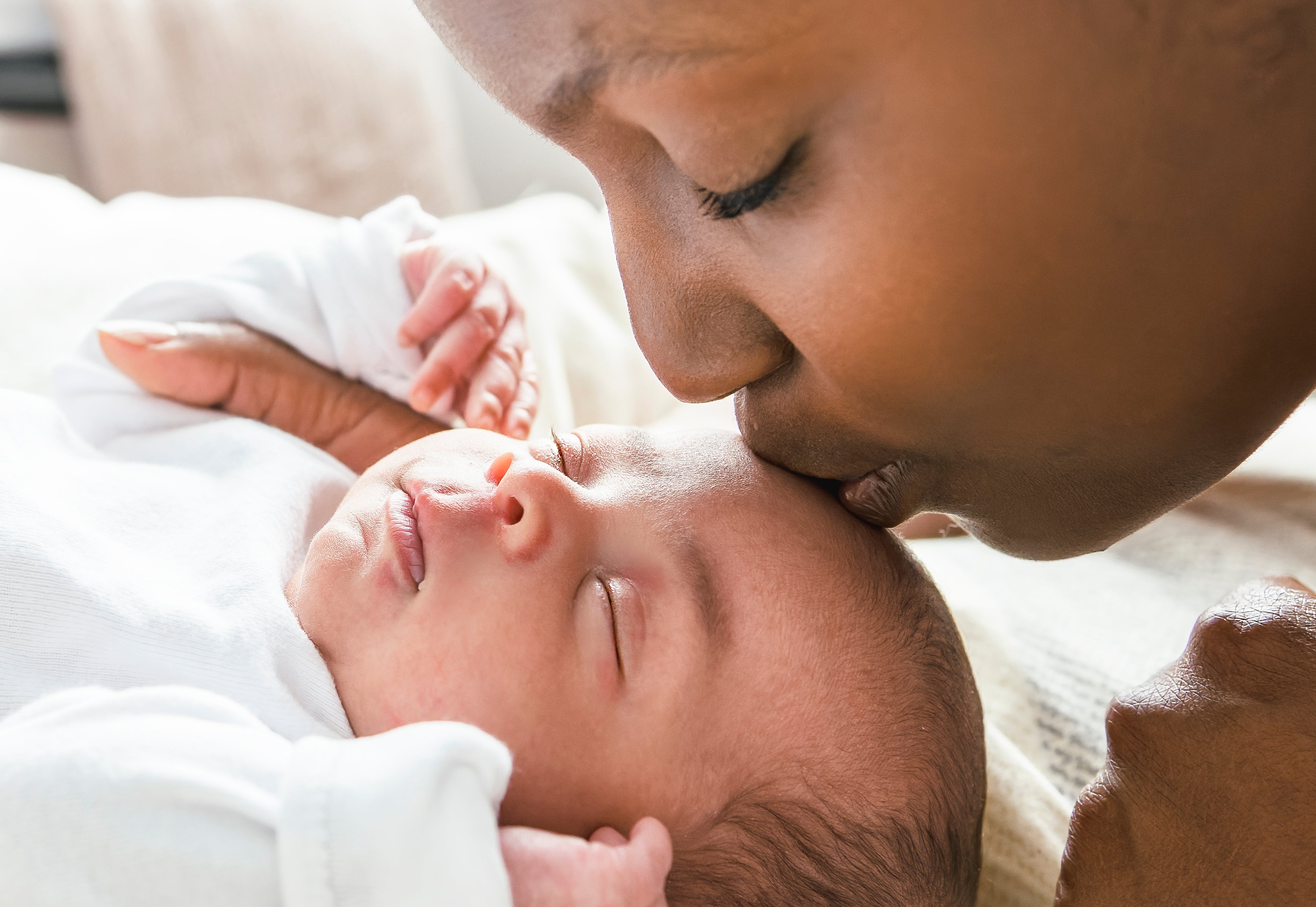 A idiosyncratic mildly kisses a sleeping baby's forehead, showing a tender moment
