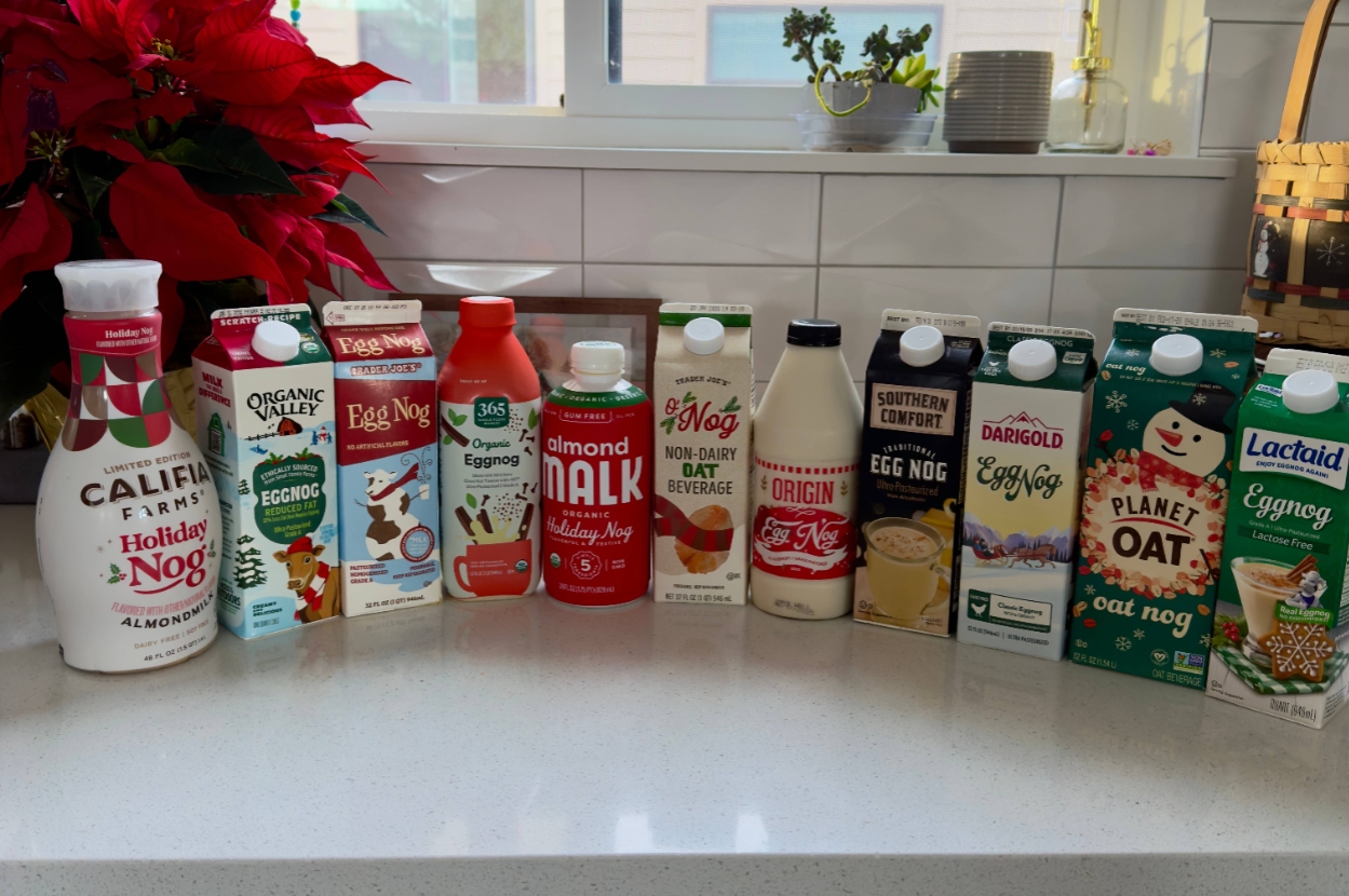 A variety of holiday nog cartons, including almond, oat, and traditional options, arranged on a kitchen counter