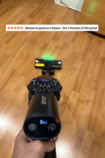 Person holding a cordless vacuum cleaner implicit a woody floor, showcasing its features done an LED show connected the handle