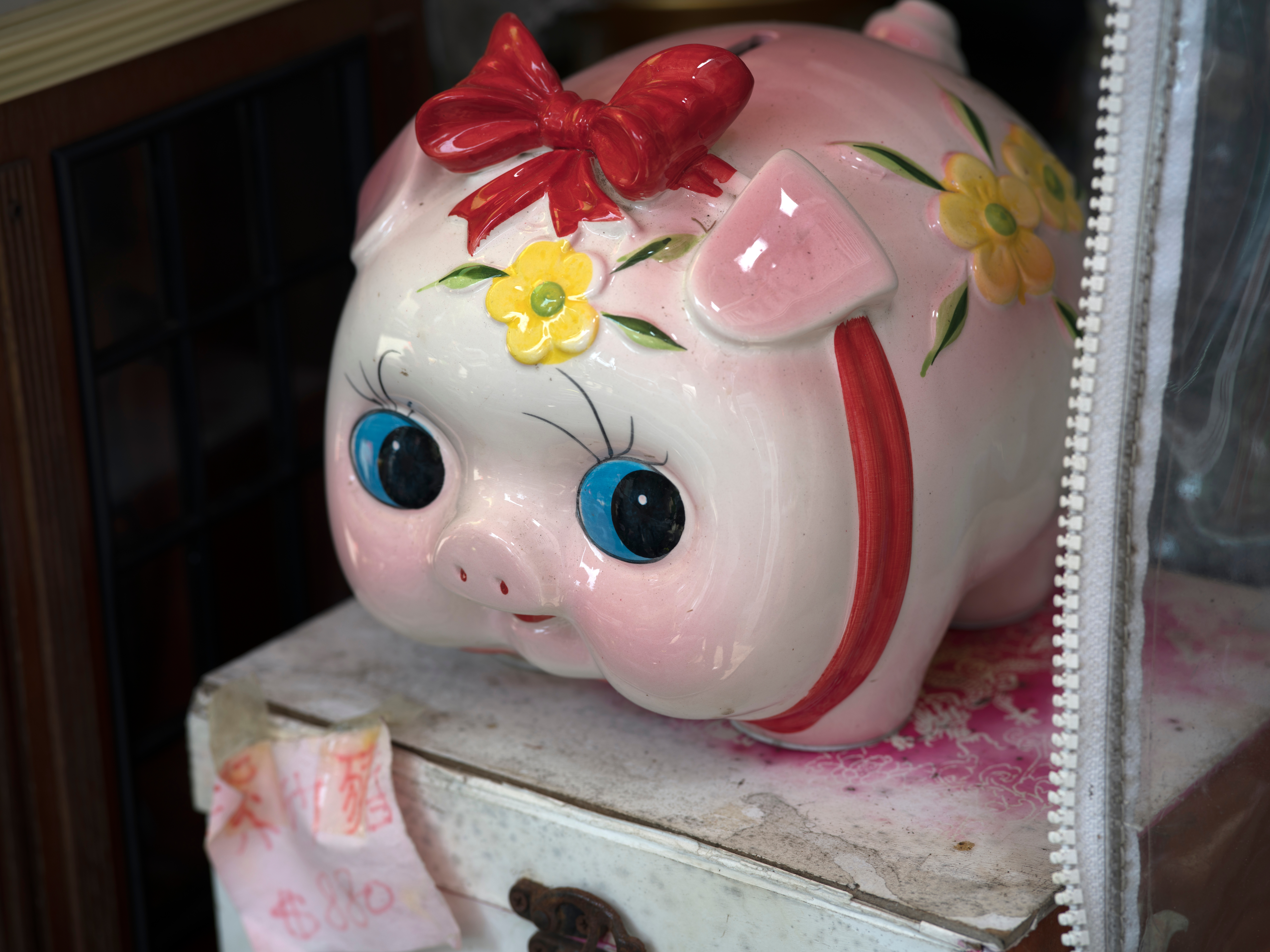 大きな目と赤いリボンの陶器製の貯金箱が、台の上に置かれている。