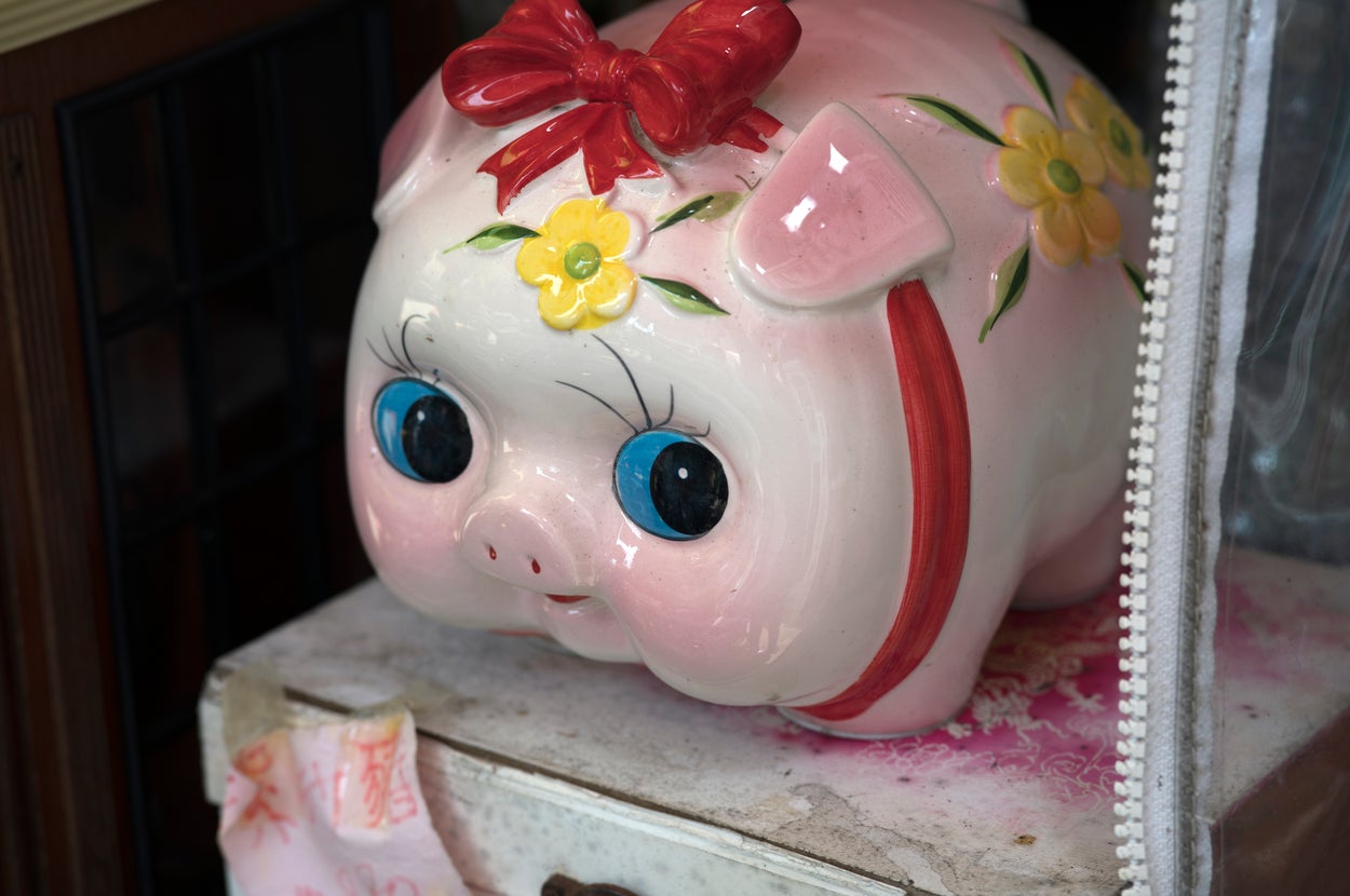 大きな目と赤いリボンの陶器製の貯金箱が、台の上に置かれている。