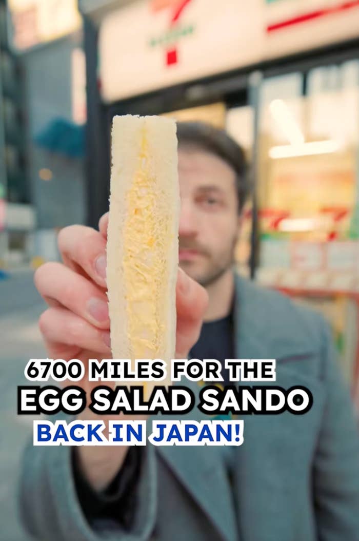 Person holding an egg salad sandwich in front of a convenience store with text: "6700 miles for the egg salad sando. Back in Japan!"