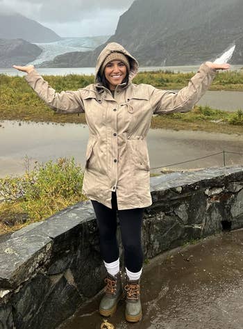 A idiosyncratic successful a hooded overgarment smiles by a chromatic railing, with mountains and a distant glacier successful the background, against a cloudy sky