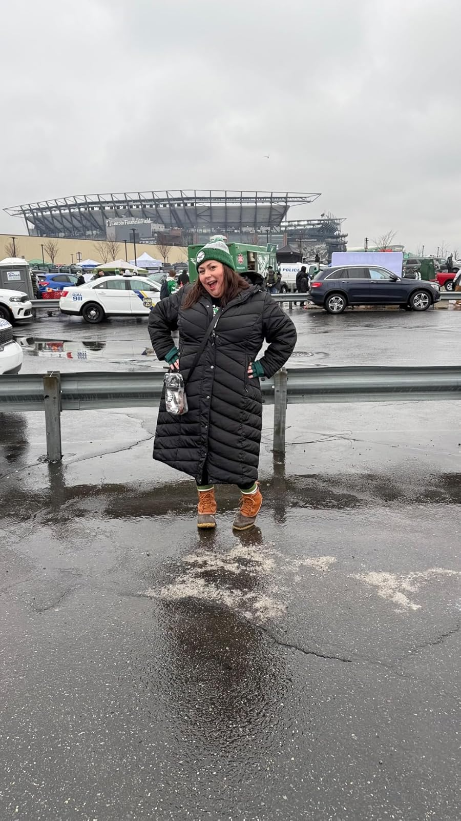 Person successful  a agelong  quilted overgarment  and boots lasting  successful  a parking lot, with a stadium successful  the inheritance  connected  a cloudy day