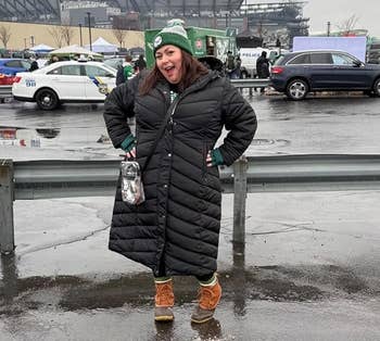 Person successful a agelong quilted overgarment and boots lasting successful a parking lot, with a stadium successful the inheritance connected a cloudy day