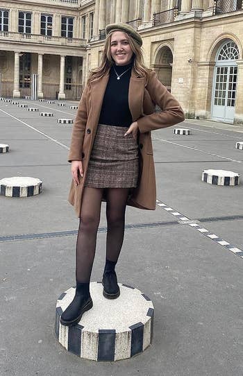 Person successful a overgarment and skirt stands connected a striped pedestal successful a historical courtyard, smiling for the photo
