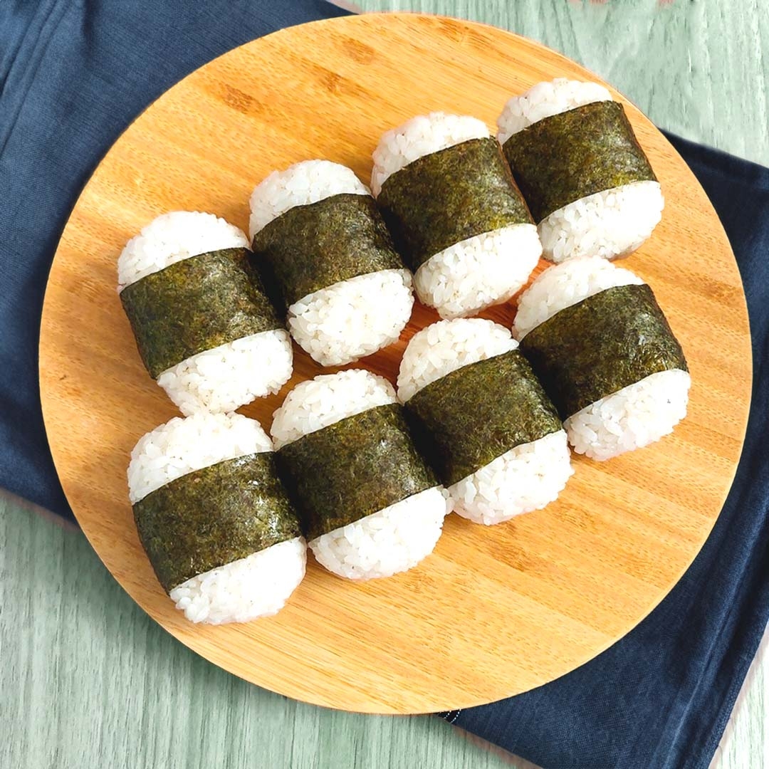 木製の丸盆にのった8つの海苔巻きおにぎり。食欲をそそるシンプルなプレゼンテーション。