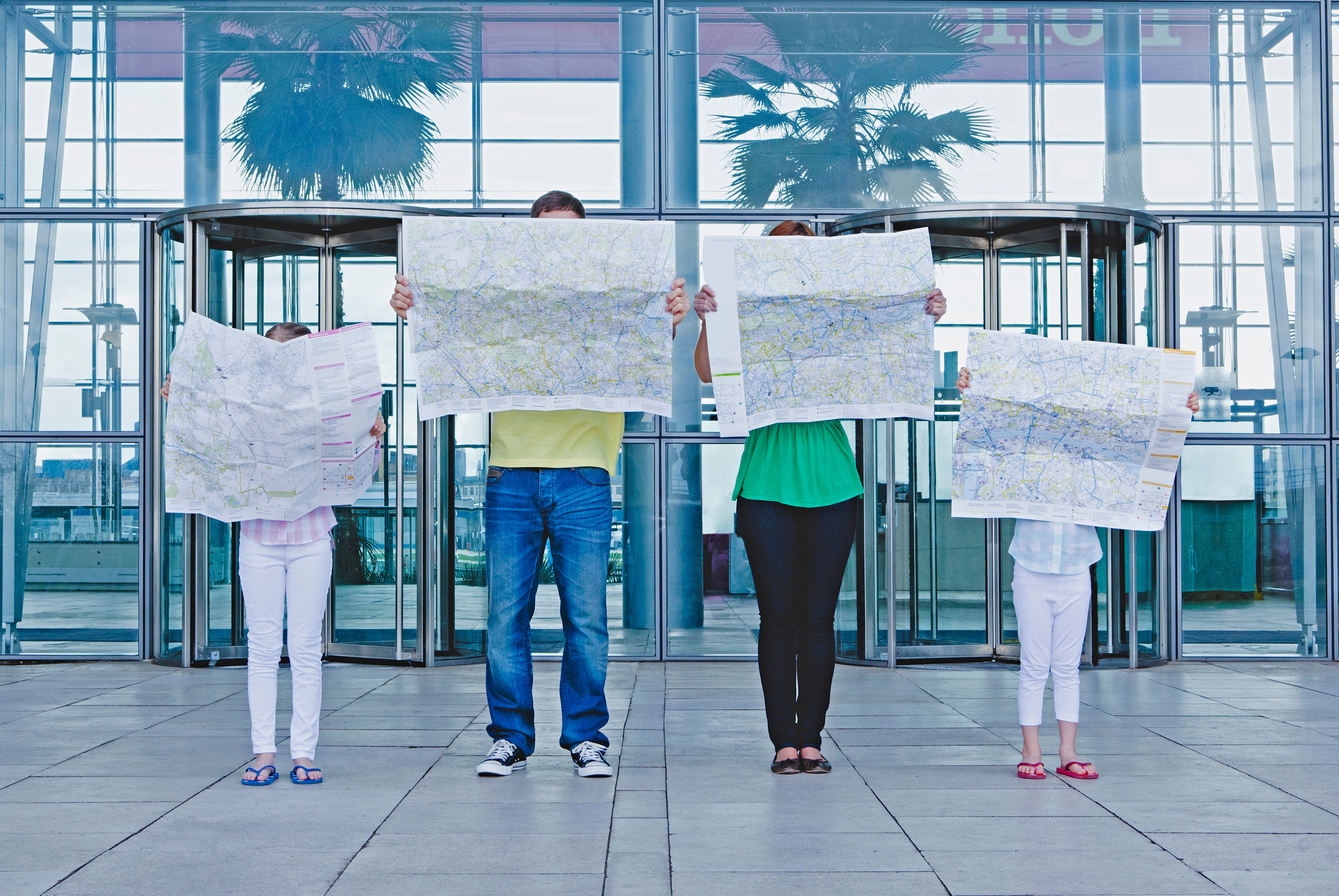 Family of 4 stands successful beforehand of solid gathering holding ample maps, covering their faces. Palms and modern architecture disposable successful the background