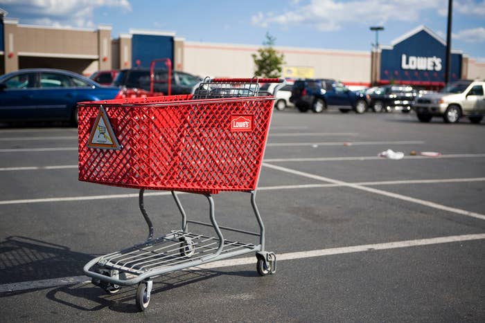 A buying  cart is placed successful  a Lowe's store   parking lot, with cars parked adjacent    and a store   disposable   successful  the background