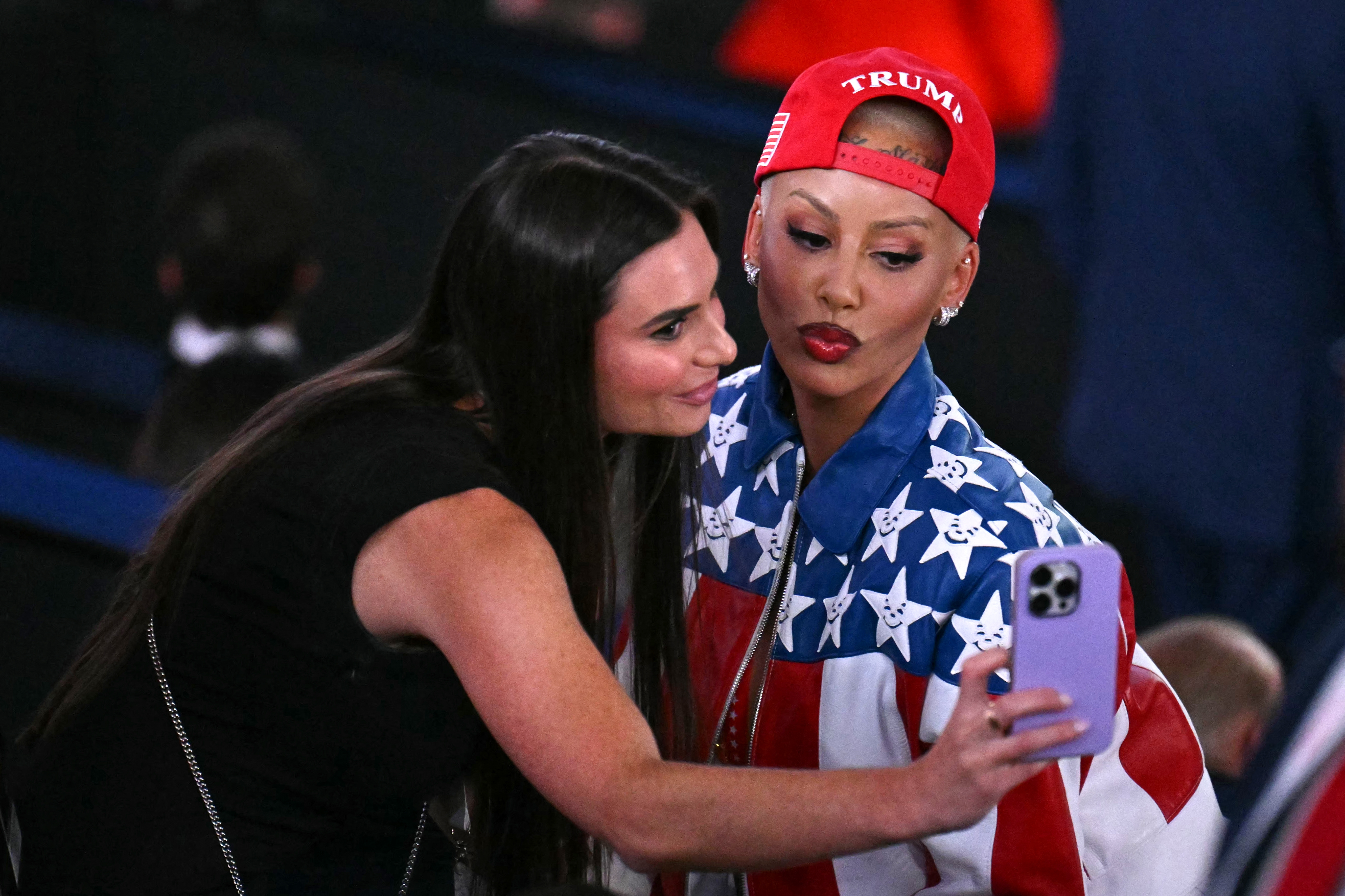 Two individuals taking a selfie. One wears a star-patterned overgarment   and a cap