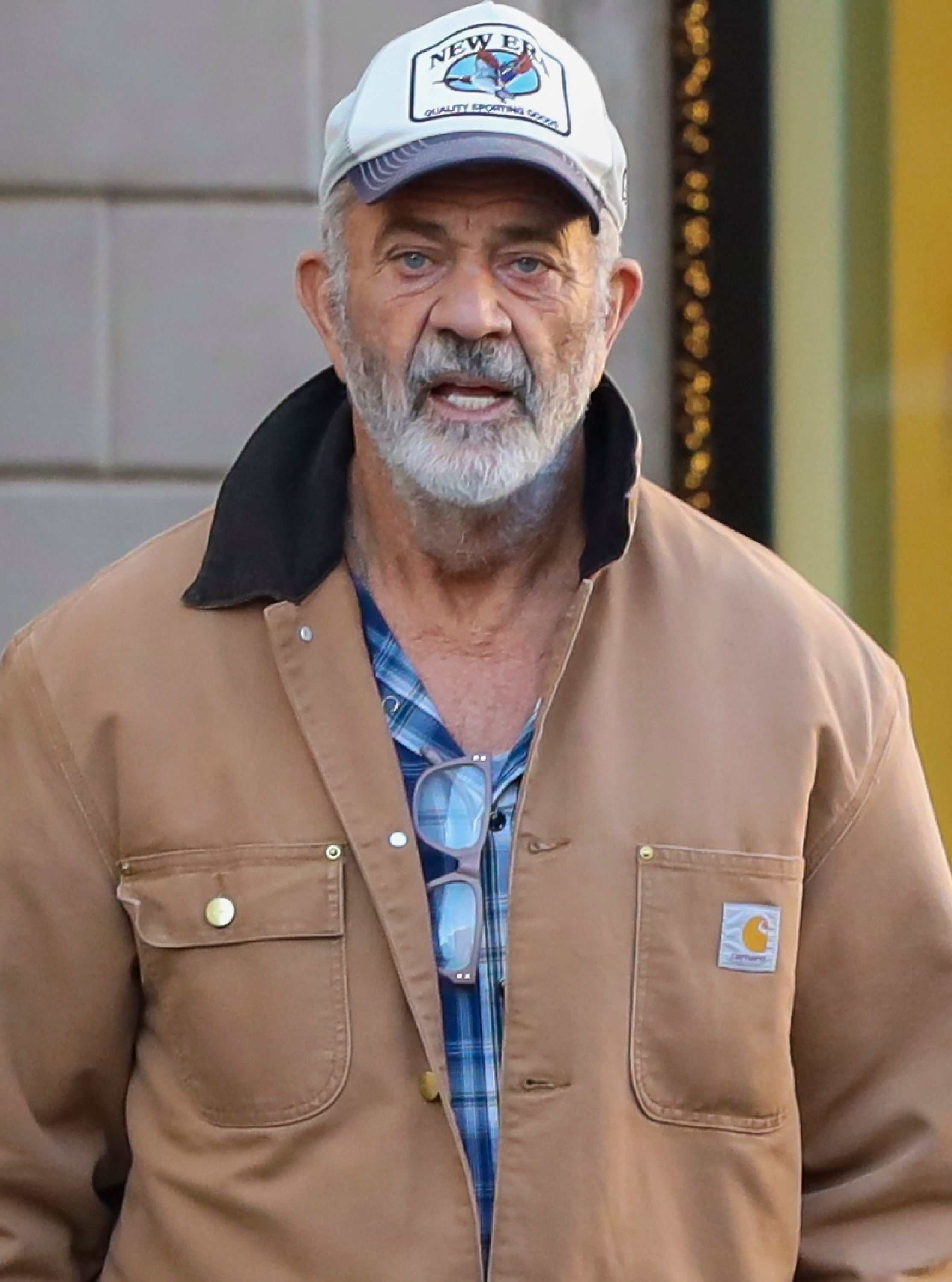 A bearded antheral   successful  a casual jacket, plaid shirt, and headdress  stands outdoors, looking straight  astatine  the camera